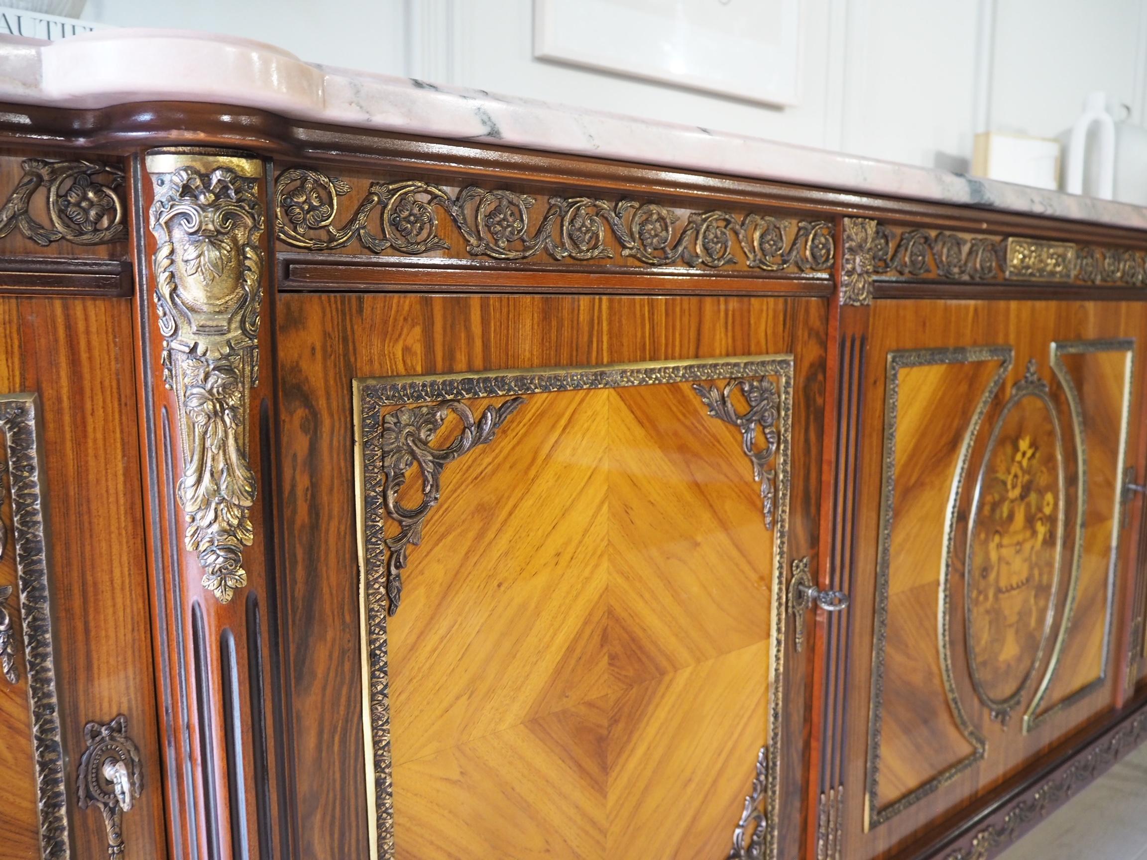 A beautiful French Louis XVI style mahogany sideboard made by JP Ehalt (name inside left cabinet), circa 20th century with a marble top, above the body where there are lovely elaborate marquetry inlays, featuring flower vases.


It has gilt metal