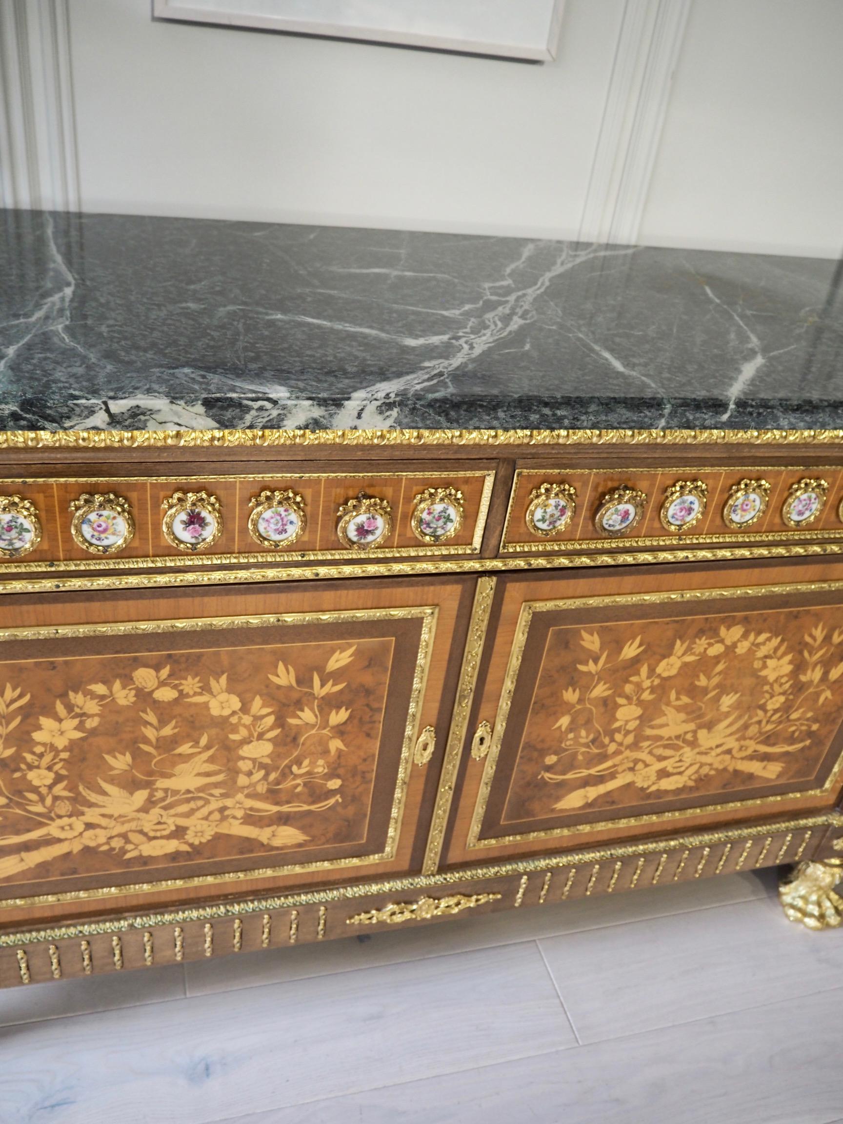 A Louis XVI style bow fronted marble topped sideboard with two frieze drawers with Sevres style floral plaques above storage base and two side cabinets. 

Ormolu mounted edges and acanthus and paw feet to sides, front and back. Walnut inlaid front