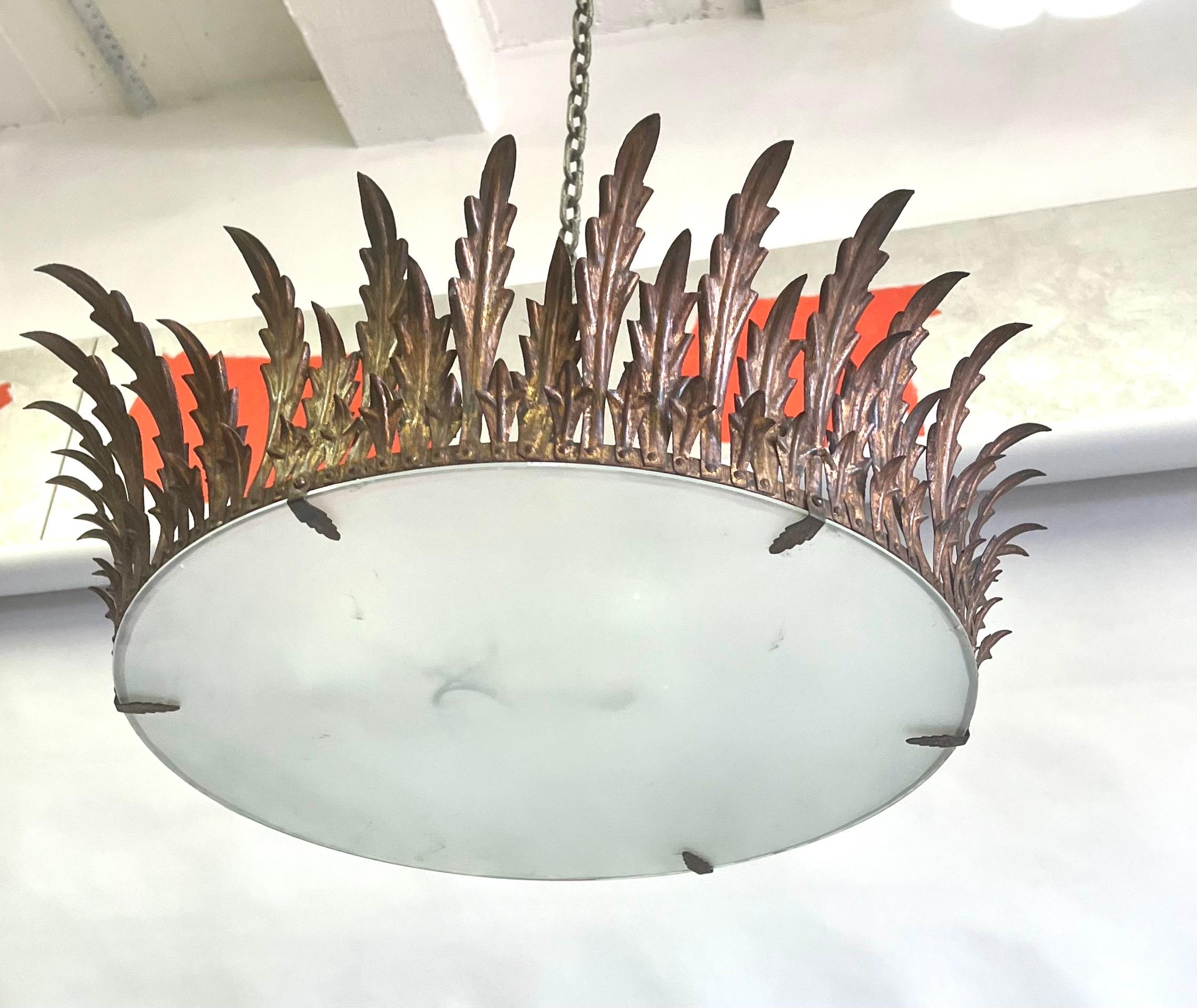 A Large French Mid-Century Modern Gilt Iron Crown or Sunburst Pendant / Chandelier /  Flush Mount in the spirit of the legendary French ironworker, Gilbert Poillerat, circa 1940. This enchanting piece is composed gilt iron acanthus leaves arranged