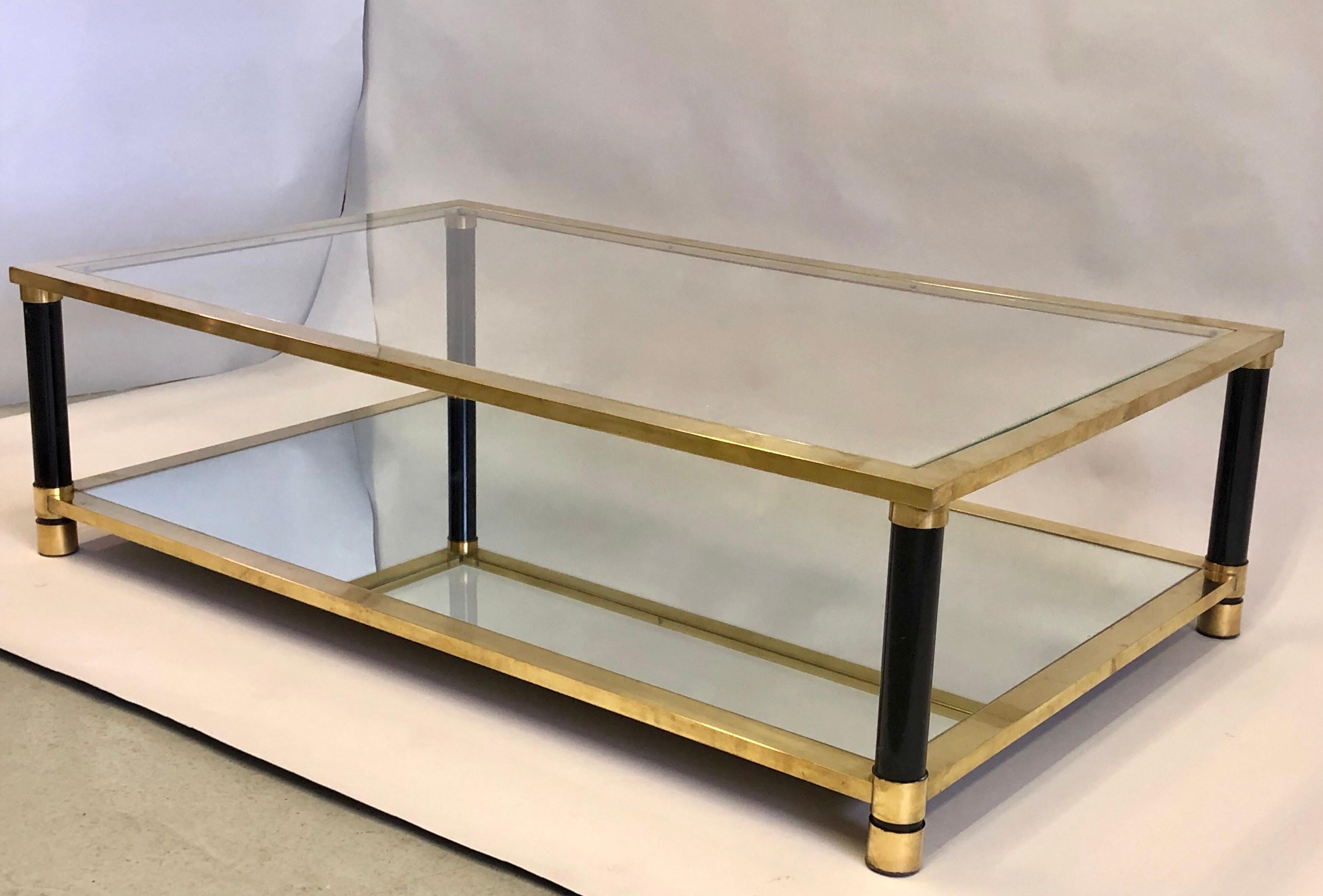 Sober, large French Mid-Century Modern double level solid brass cocktail table with partially enameled legs attributed to Maison Charles, circa 1970.

The lower level top is composed of mirror inset into the frame and the upper level of clear