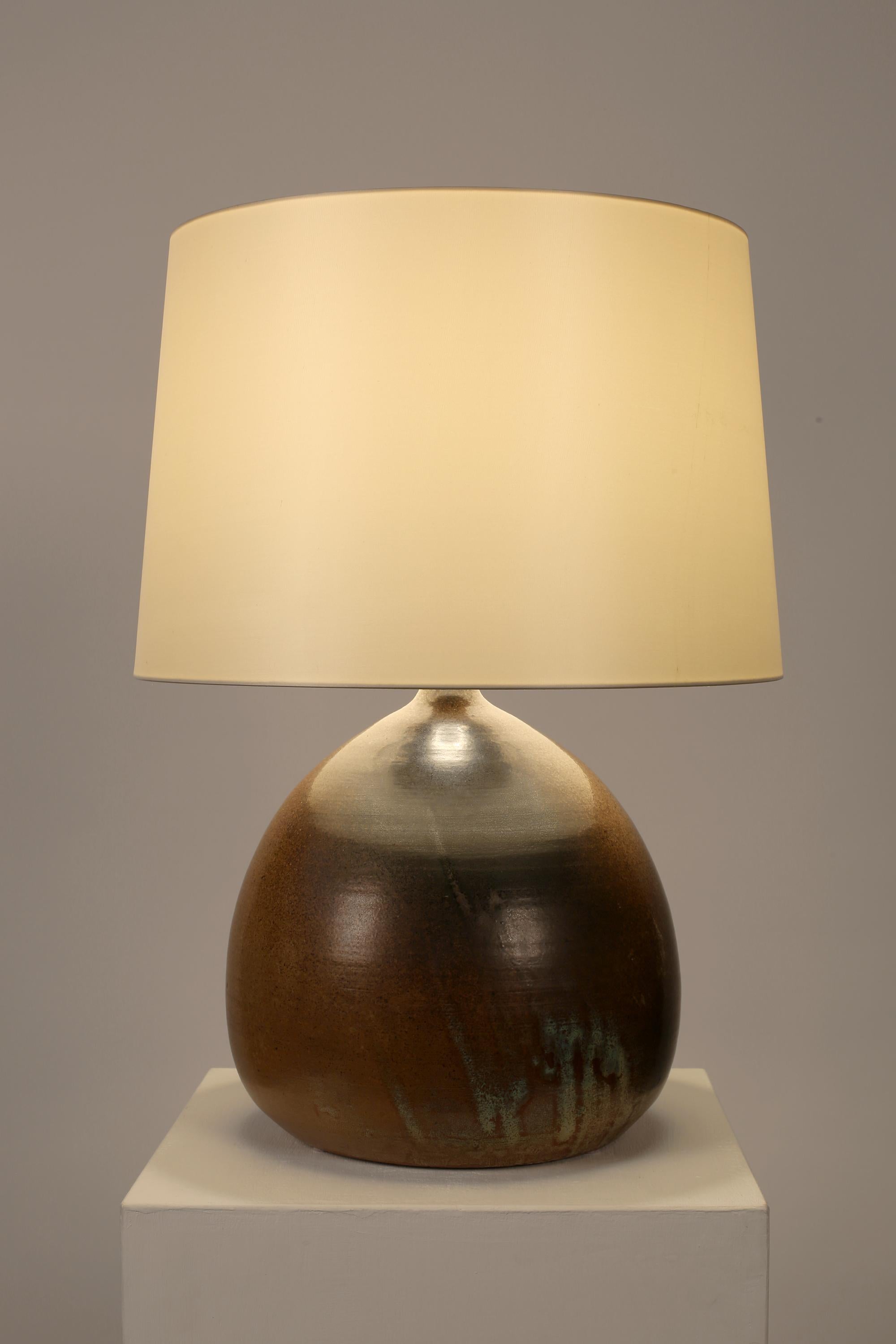 Une lampe de table monumentale en grès de forme bouteille avec une glaçure terreuse. Français, c. 1960. Livré avec un abat-jour en soie dupion blanc cassé.