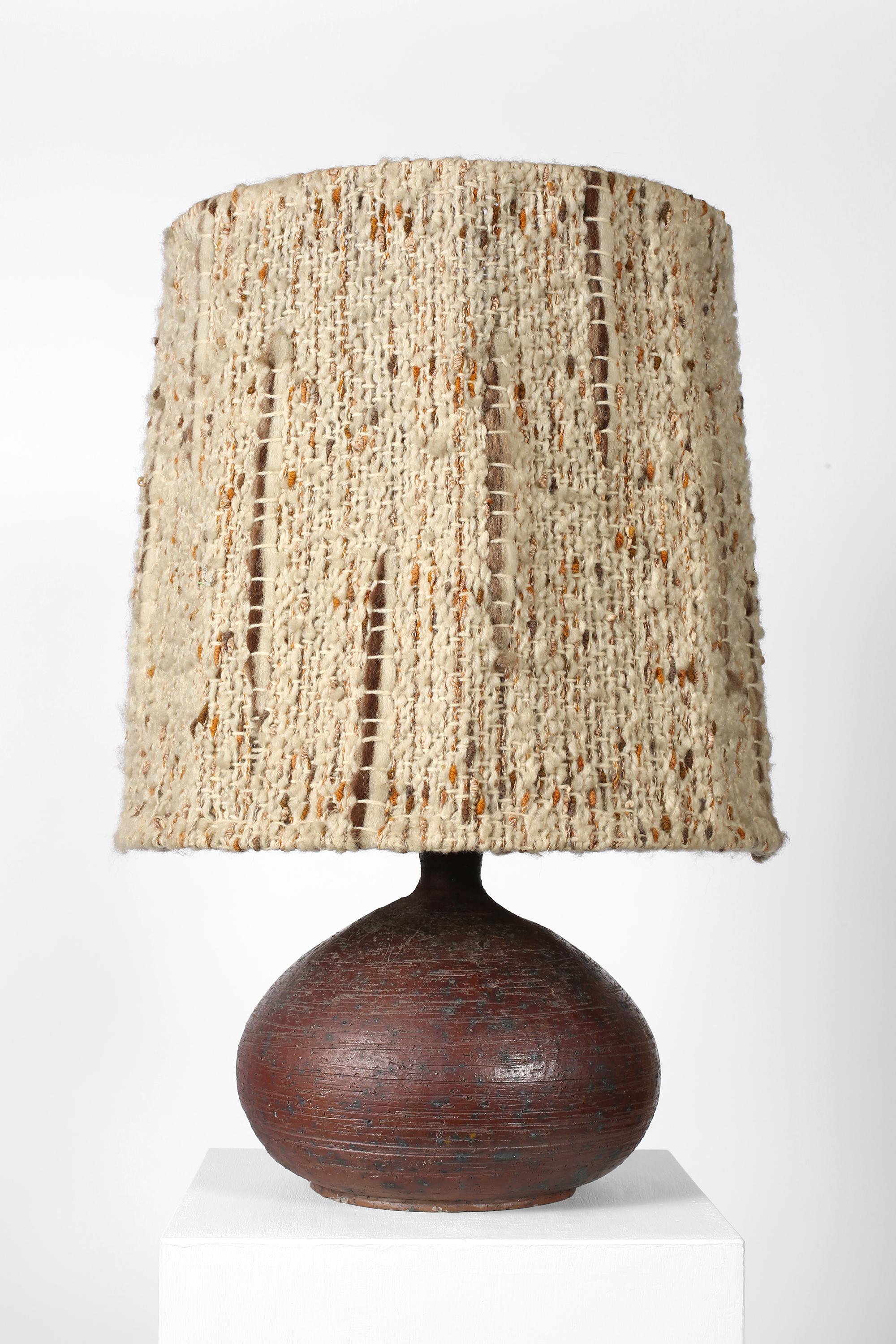 Lampe de table en grès gravé du milieu du 20e siècle, de forme trapue et semblable à une bouteille. Avec son grand abat-jour en laine tissée d'origine, signé indistinctement au dos de la base. Français, c. 1960. 