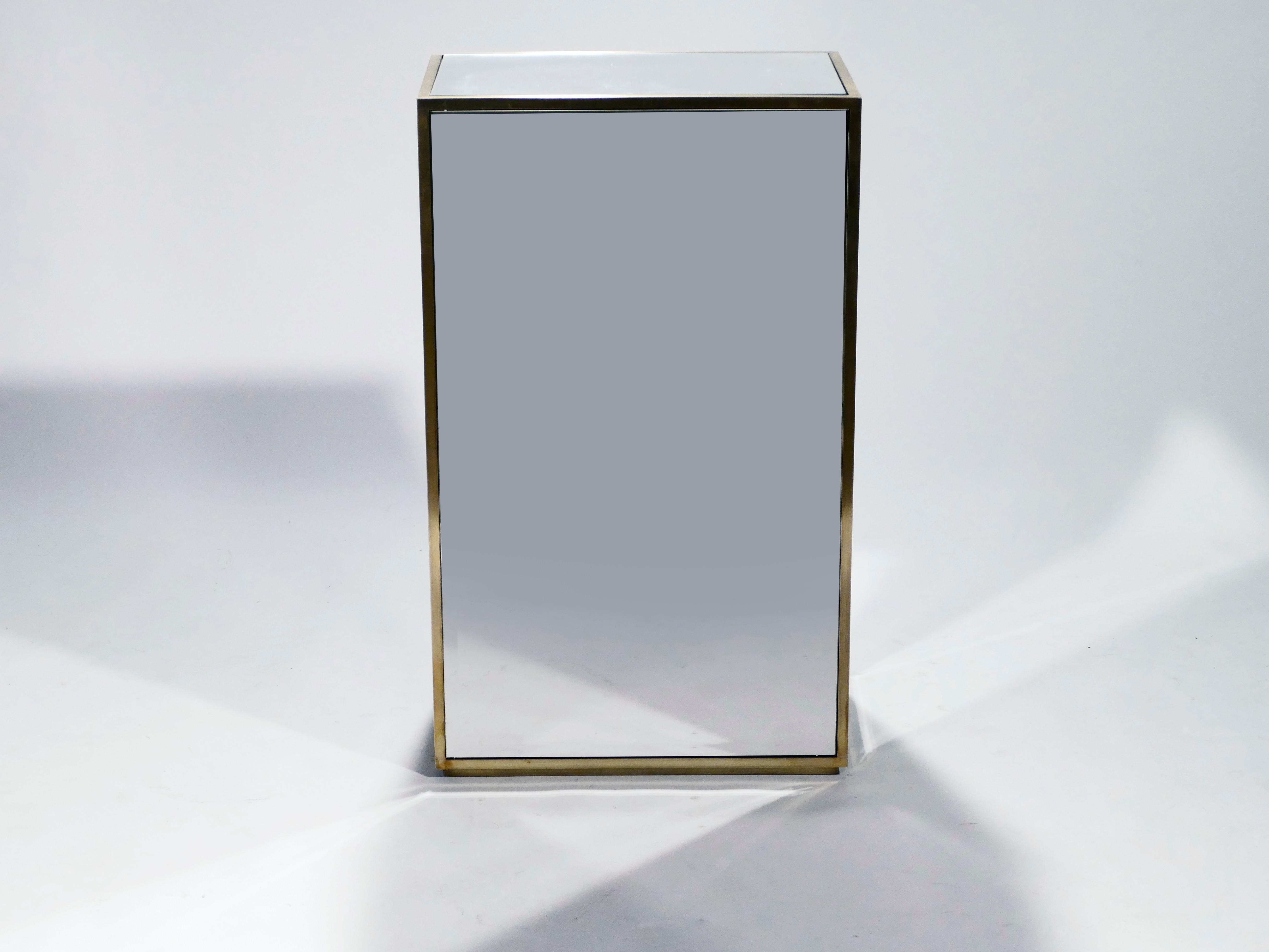 This mirrored glass and brass pedestal from the 1970s is significant in weight and size. It’s panelled in well-made, bevelled reflective glass on five of its six sides. Each panel is slightly raised from the brass border. The piece is distinctively