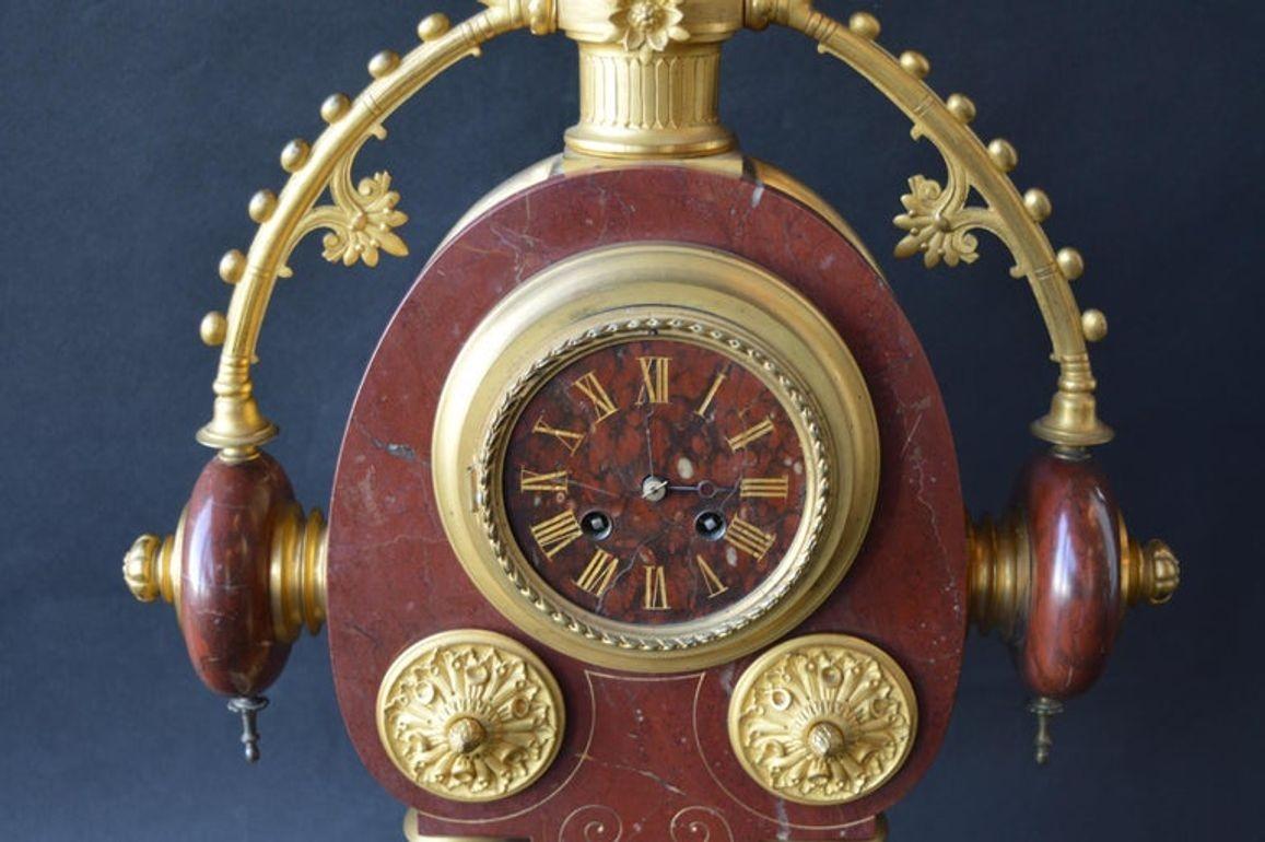 A striking and unusual French Neo-Grec Revival mantel clock, circa 1870, featuring a richly veined rouge griotte marble case adorned with gilt bronze mounts. The arched body is centered by a circular dial with gilt Roman numerals and Breguet hands,