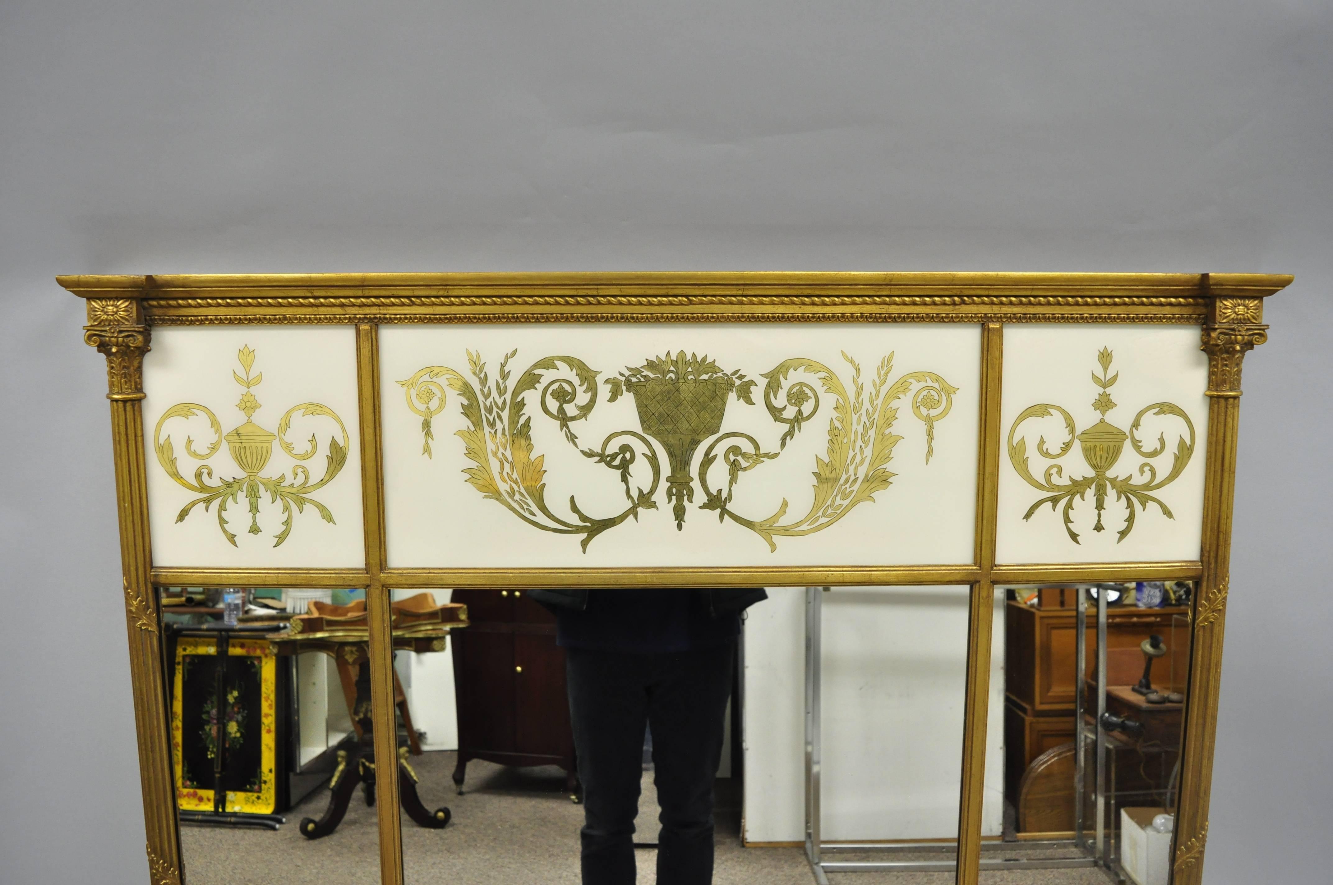 Large French neoclassical style gold gilt reverse painted Italian trumeau wall mirror. Item features a three section wooden frame, reverse painted glass pediment with urn, drape, and floral scroll work, and large impressive form, circa mid-20th