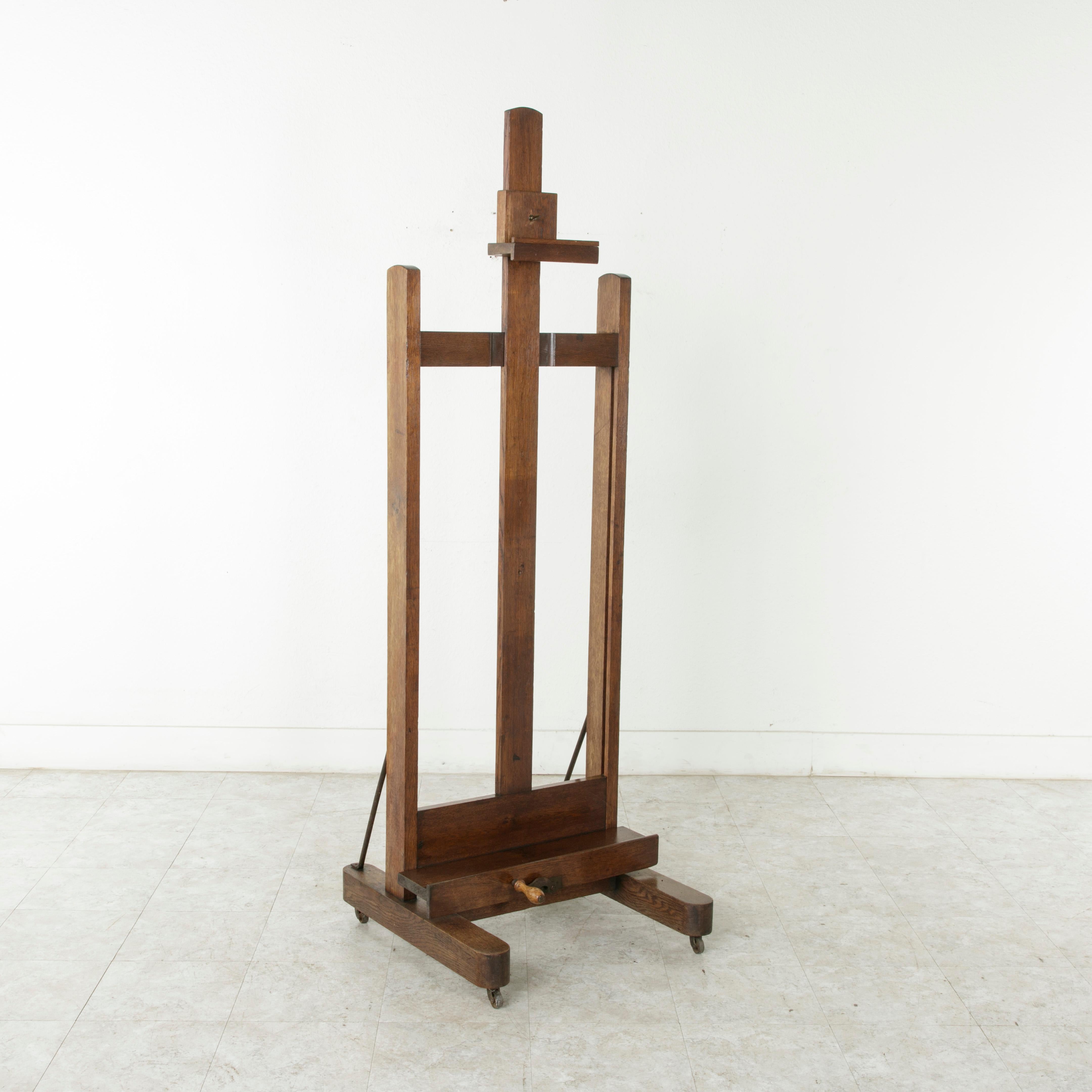 This large French oak artist's floor easel from the turn of the 20th century features a functioning iron crank and mechanism allowing for an adjustable height of 72.5 to 112.5 inches. It's five inch deep tray makes it suitable for displaying deep
