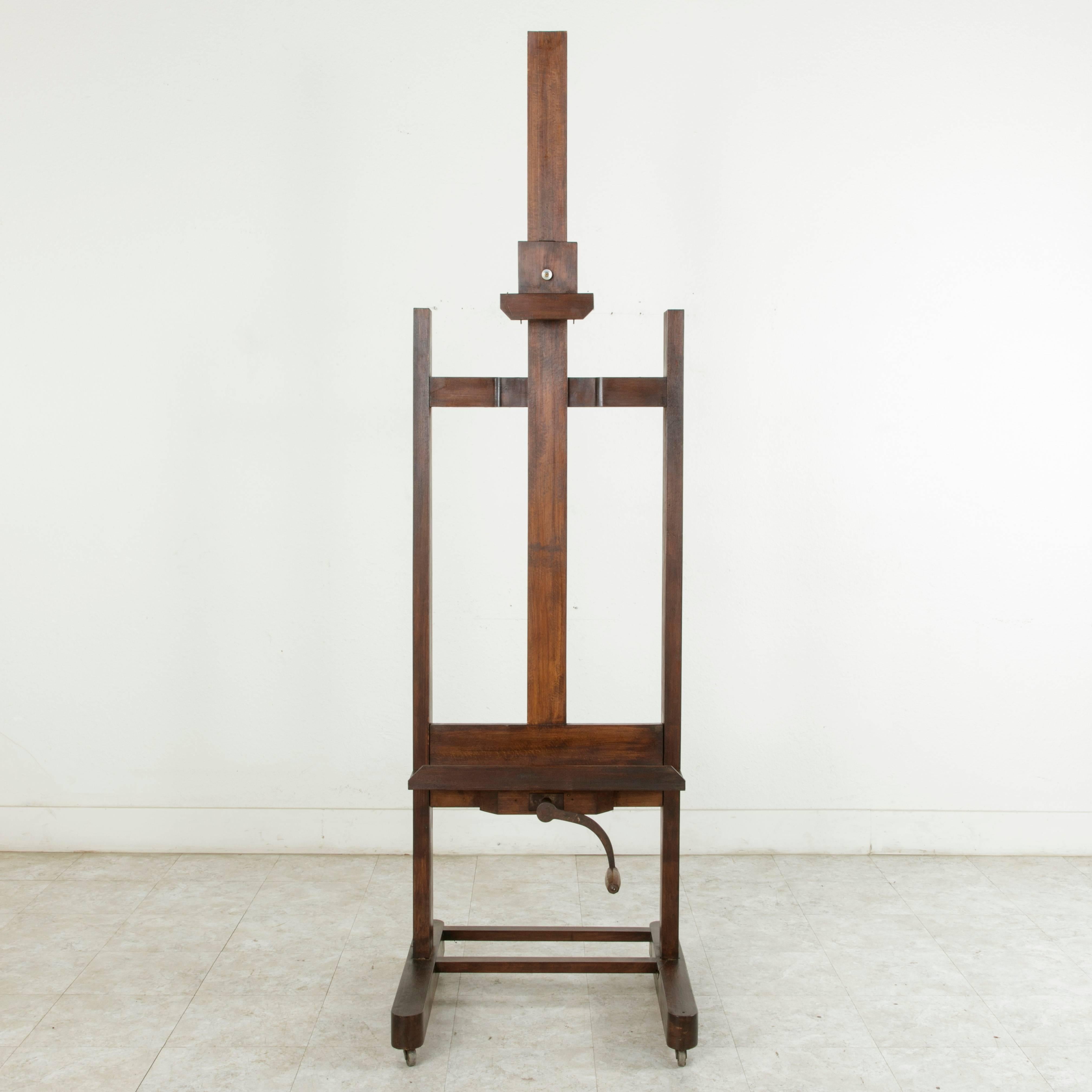 This large French oak floor easel from the turn of the 20th century features its original functioning iron crank and mechanism allowing for an adjustable height of 79 to 115 inches. It's four and a half inch deep tray makes it suitable for