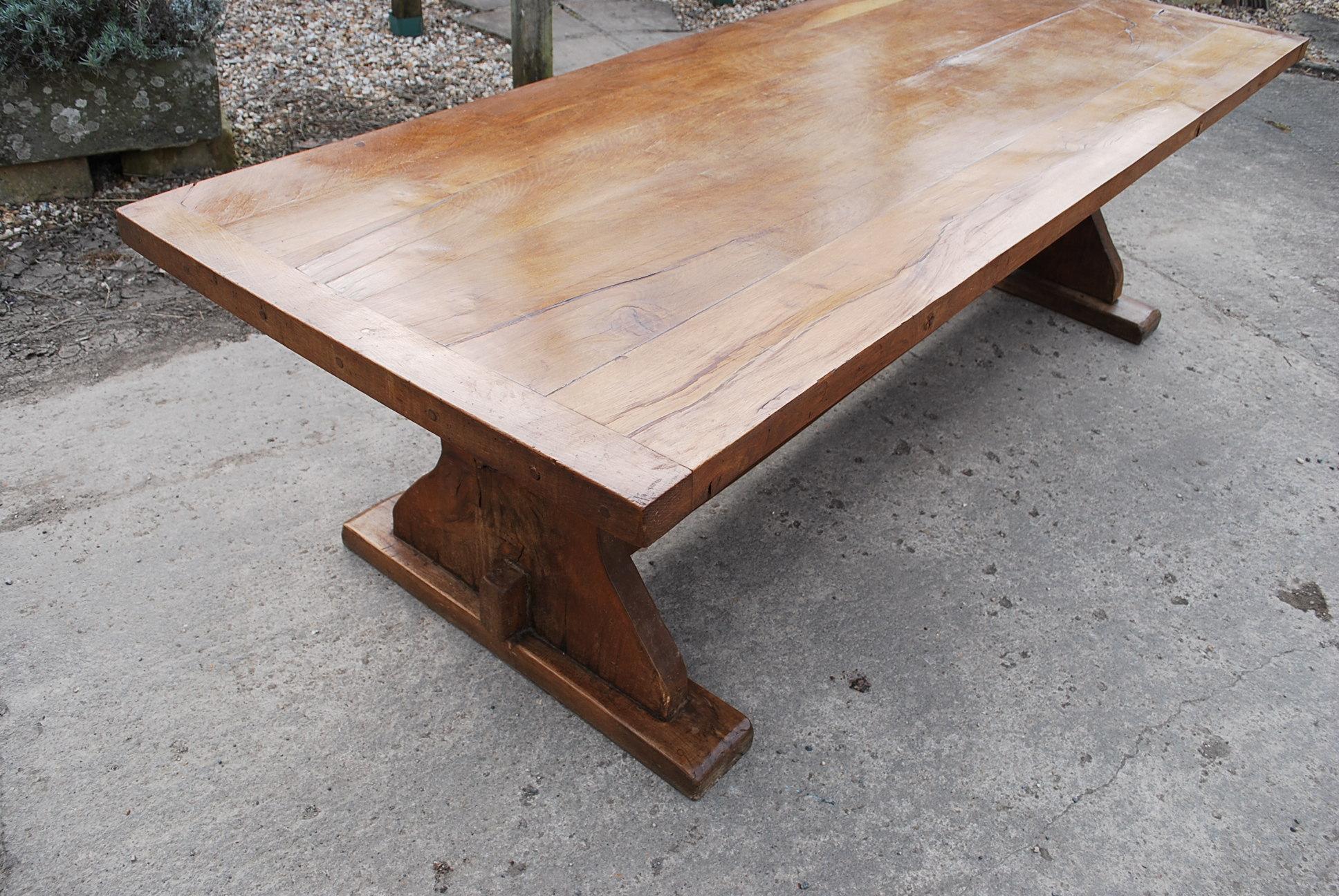 A substantial solid oak French farmhouse table of good bold proportions. Standing on solid shaped trestle ends with a low stretcher. The top is bookmatched oak boards with breadboard ends. There is a slight twist which adds to its character. Good