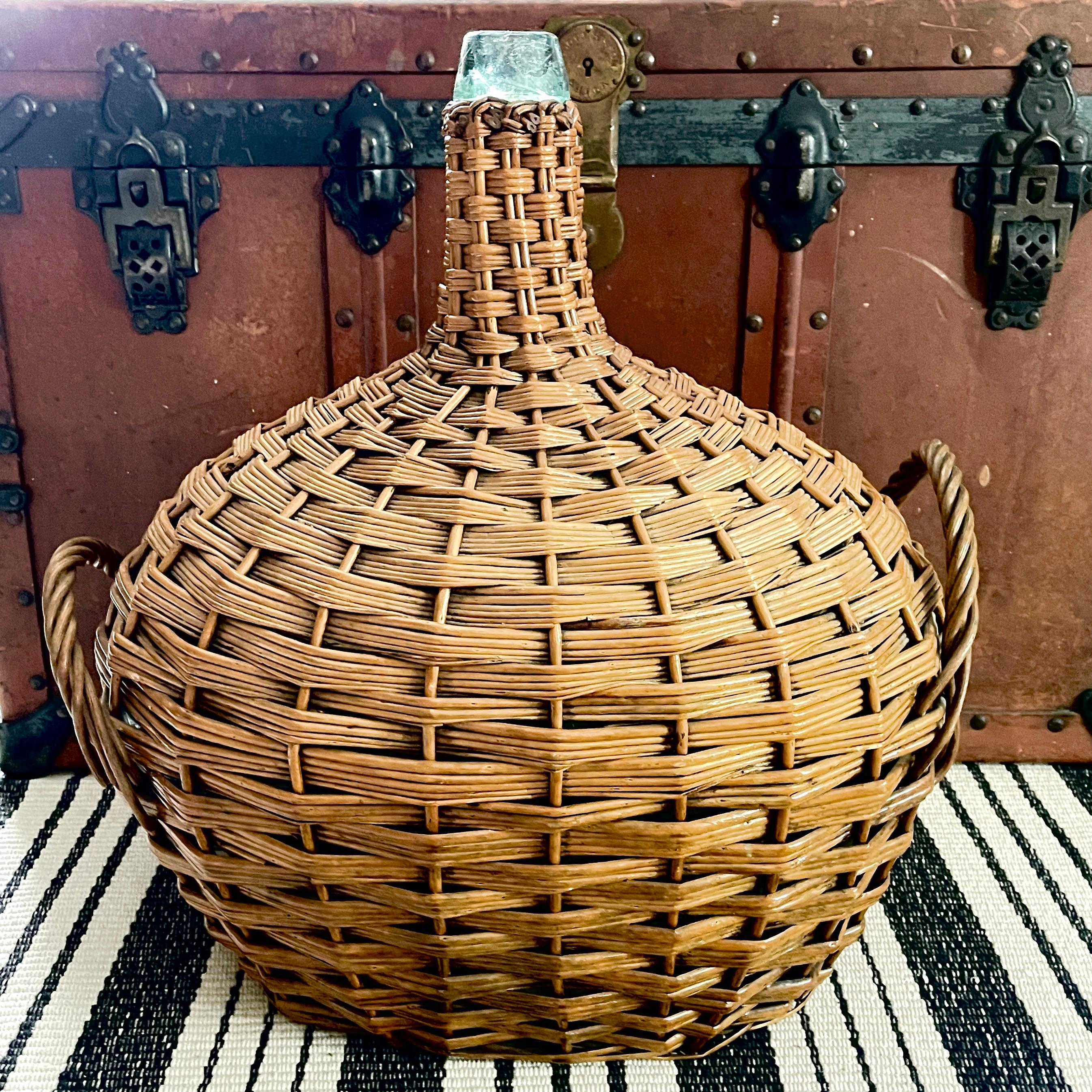 From France, a super-sized and unusual oval shaped carboy or demijohn, made up of a pale aqua colored, mouth blown glass bottle clad in a hand woven wicker casing with side carrying handles. Circa 1900.

The wicker helped protect the glass bottles
