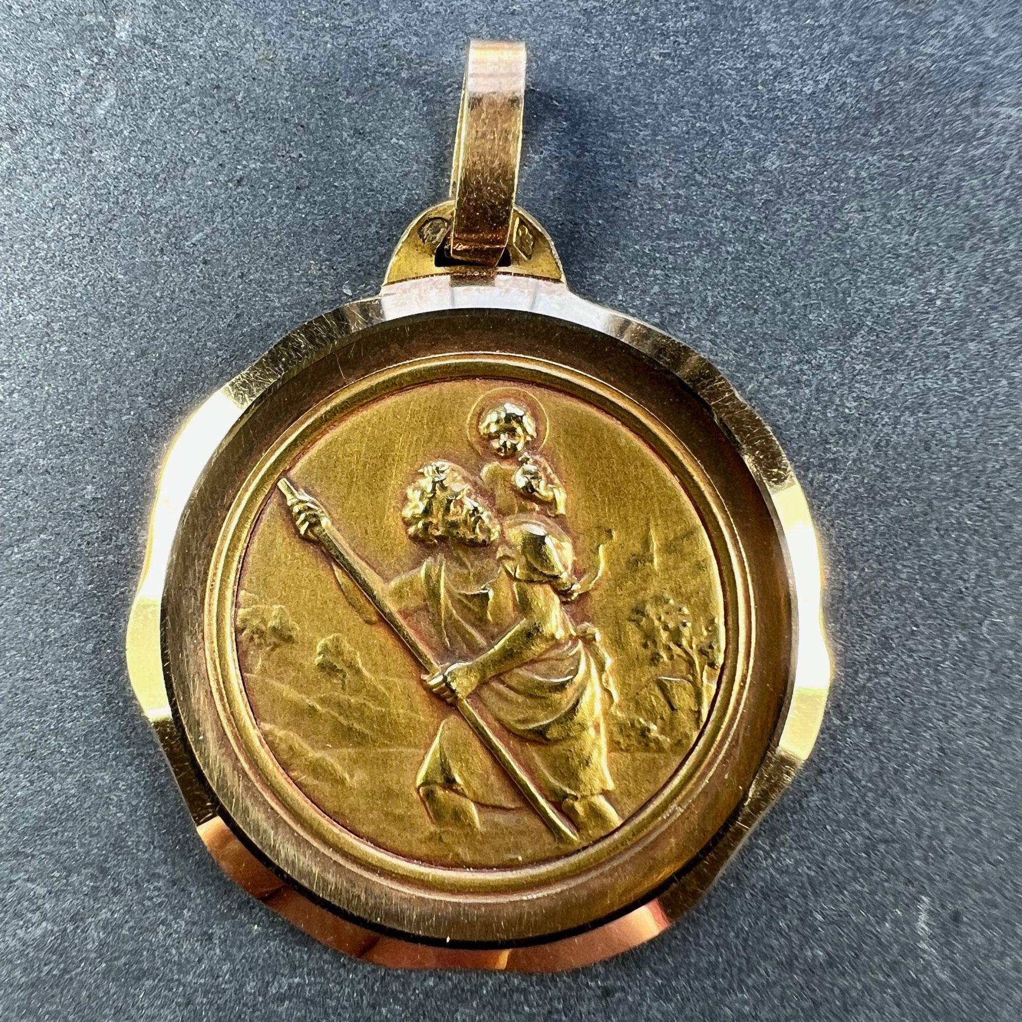 A large French 18 karat (18K) yellow gold charm pendant designed as a medal depicting Saint Christopher as he carries the infant Christ across a river, with a country landscape behind them. Set within a wavy yellow gold frame. Stamped with the