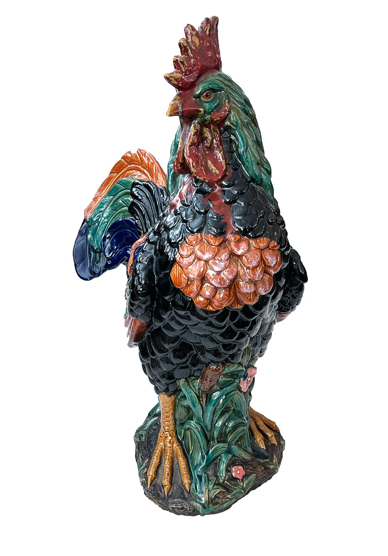 the majestic rooster with turned head and direct gaze below a proud comb all above a robust body of well-delineated plumage with feet firmly planted in a grassy ground; covered overall in rich glazes of cobalt blue, crimson, teal, black and sienna