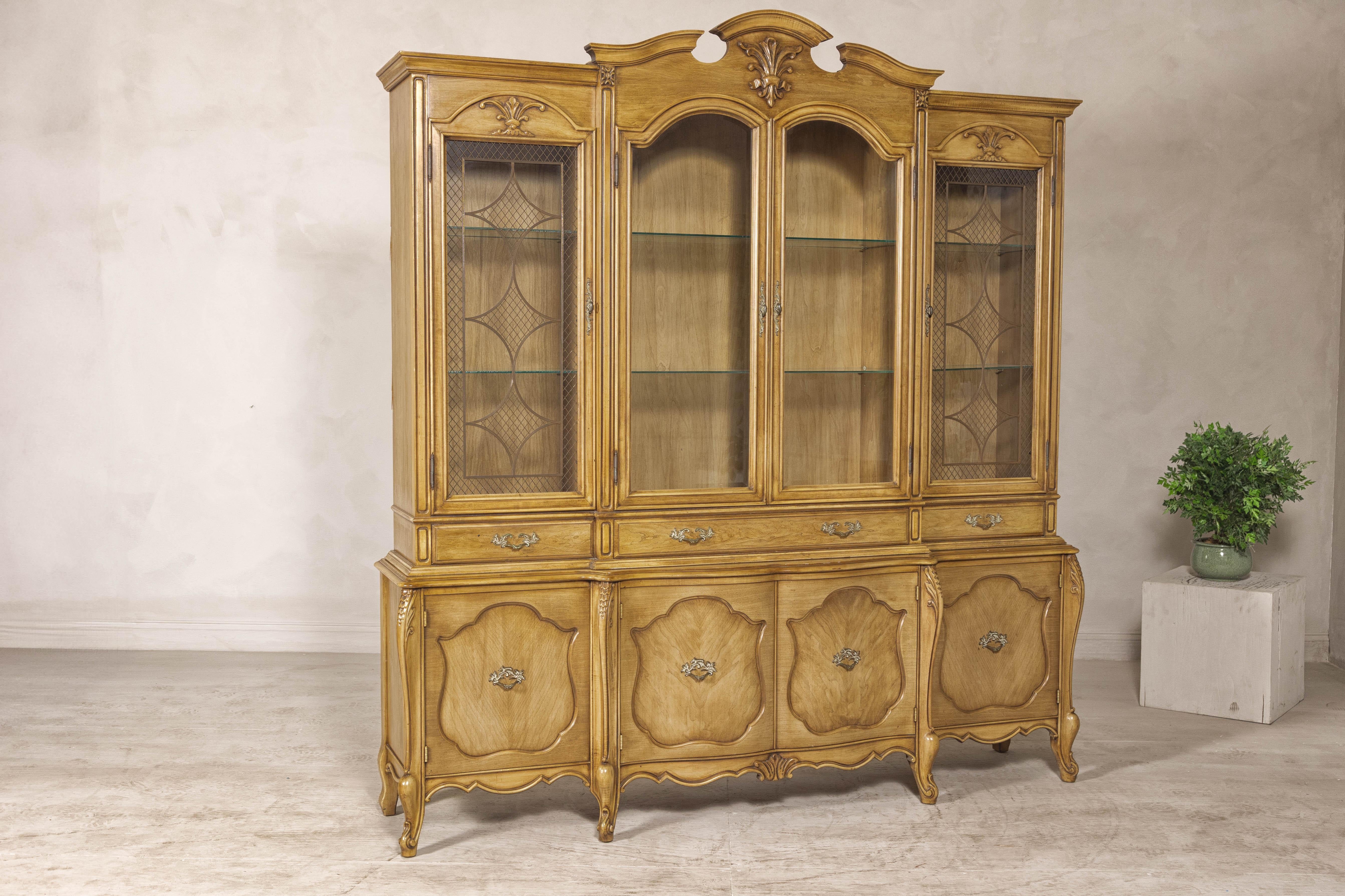 A large French Provincial style china cabinet with glass doors and arched pediment. This large French Provincial-style china cabinet combines timeless elegance with practical functionality, crafted in solid hardwood with a warm, honey-toned finish.
