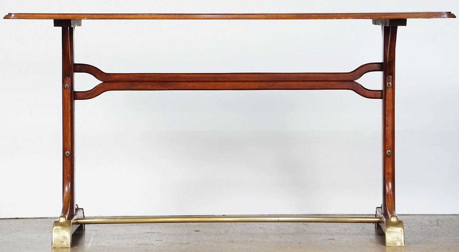 Grande table de bistrot ou de pub française au design moderniste caractéristique, avec un plateau rectangulaire en bois moulé, reposant sur une base en bois avec des renforts en laiton entre les pieds et des capuchons en laiton sur les