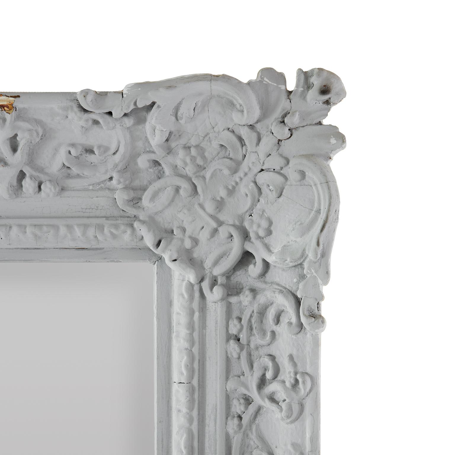 Grande specchio francese del XVIII secolo con cornice in gesso e legno decorata con volute e ornamenti floreali a pastiglia. 
Di origine francese, questo antico specchio rettangolare è stato appeso in una residenza privata del centro di Milano e