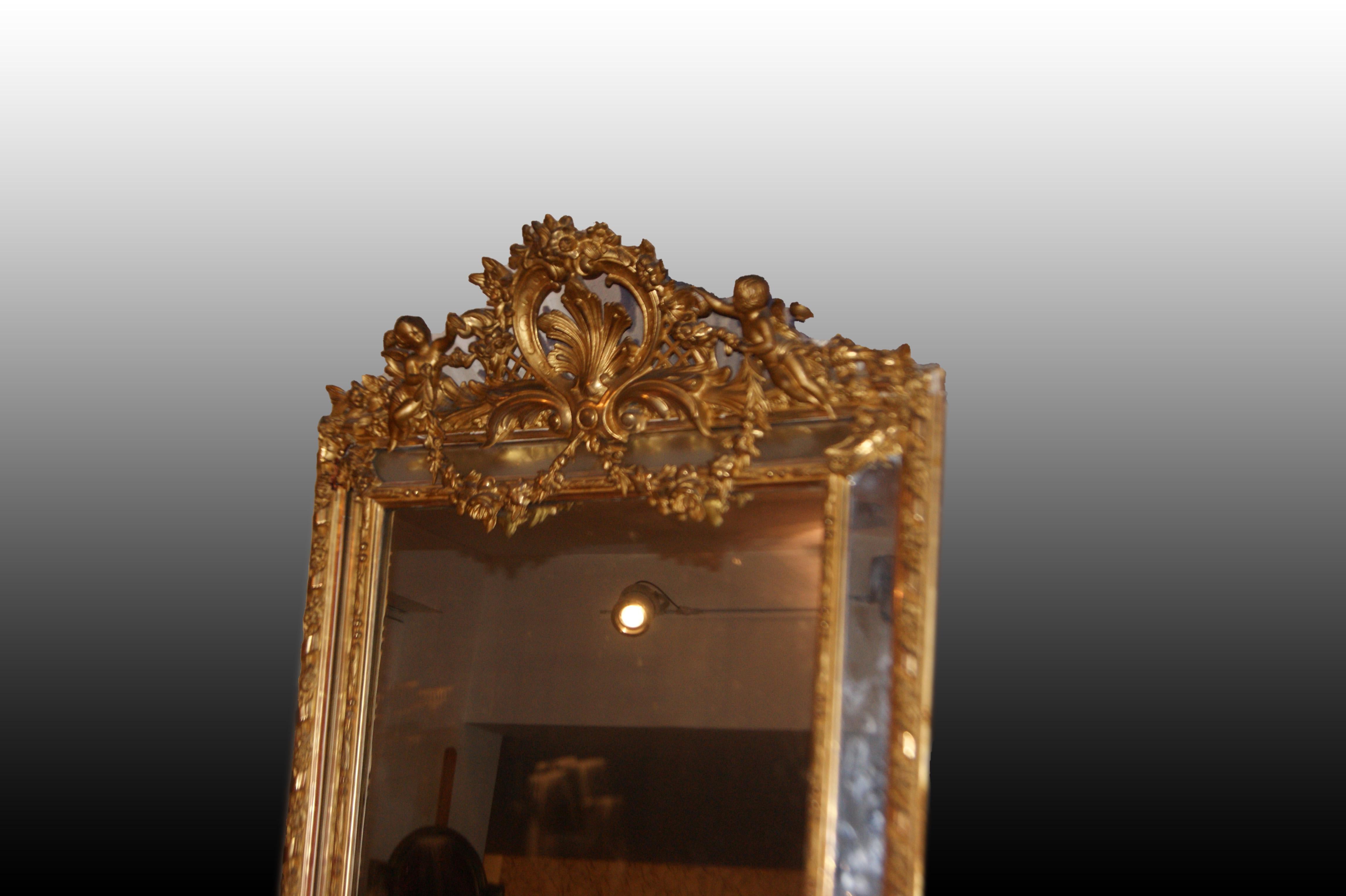 Large, rich French rectangular vertical mirror from the Mid-1800s, in the Louis XVI style, with a gilded gold leaf wooden frame. The frame is exquisitely finished with an elaborate cornice in the upper body featuring putti.

Origin: