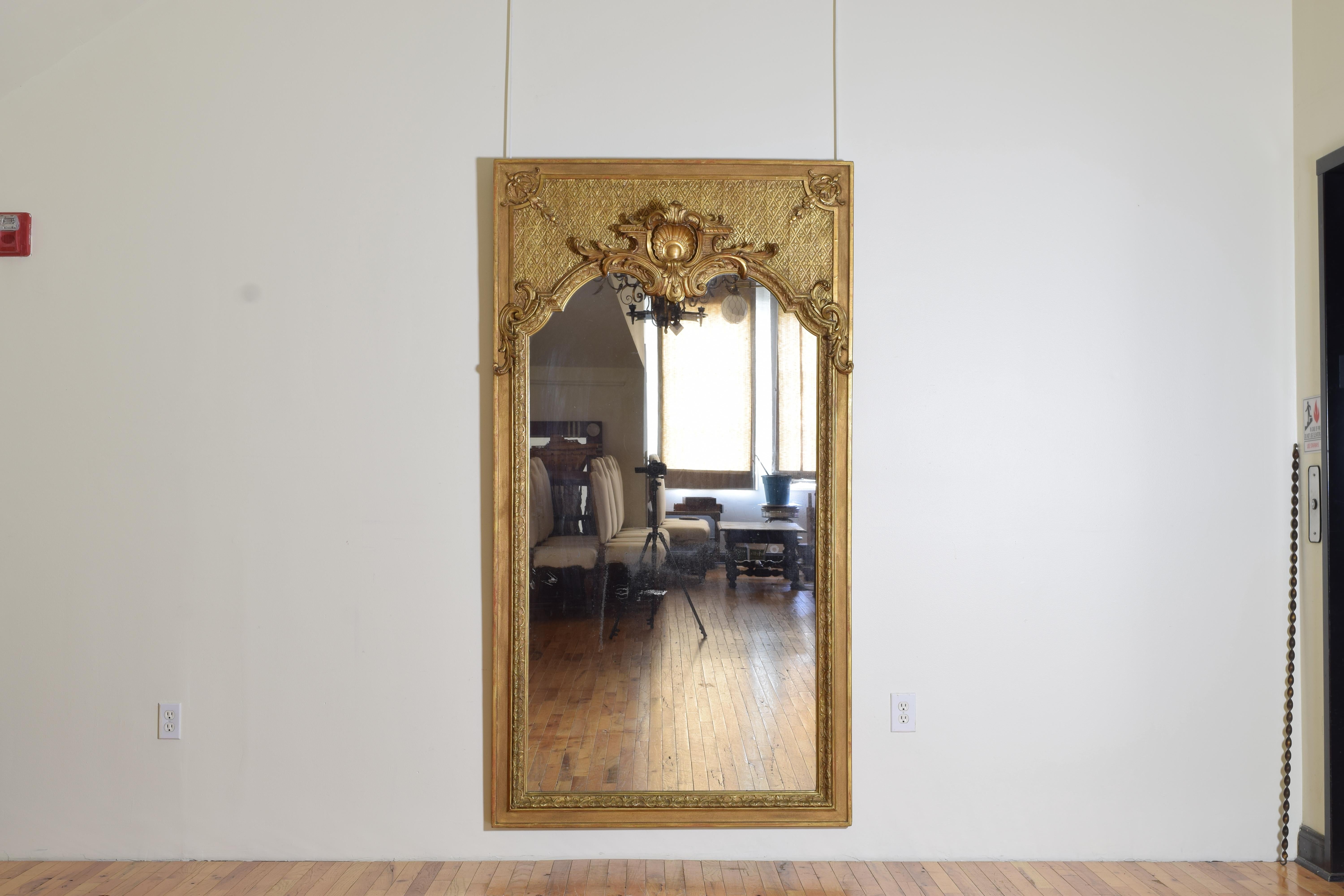 Covered entirely in 23.5 karat gold which has a slightly darker hue than 24 karat gold which appears slightly more red, this mirror incorporates elements of the French Regence period with its criss-crossed lozenge form design in the upper section