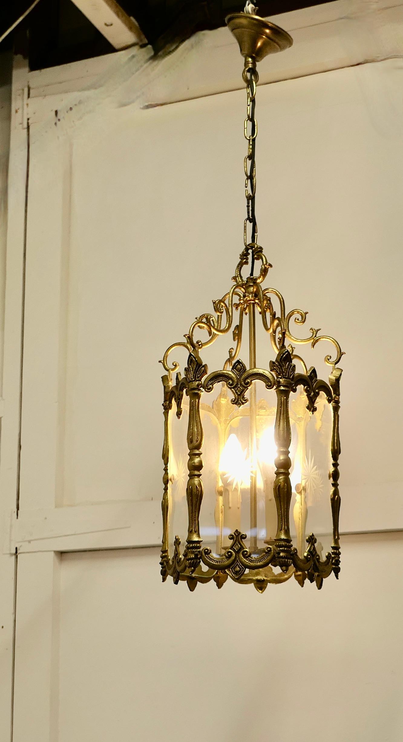 Large French Rococo brass glass lantern hall light

A superb quality heavy brass lantern, the lantern has 6 glass sides each etched with a starburst at the centre, the decorative brass is in the French style with leaves and it hangs on a chain
