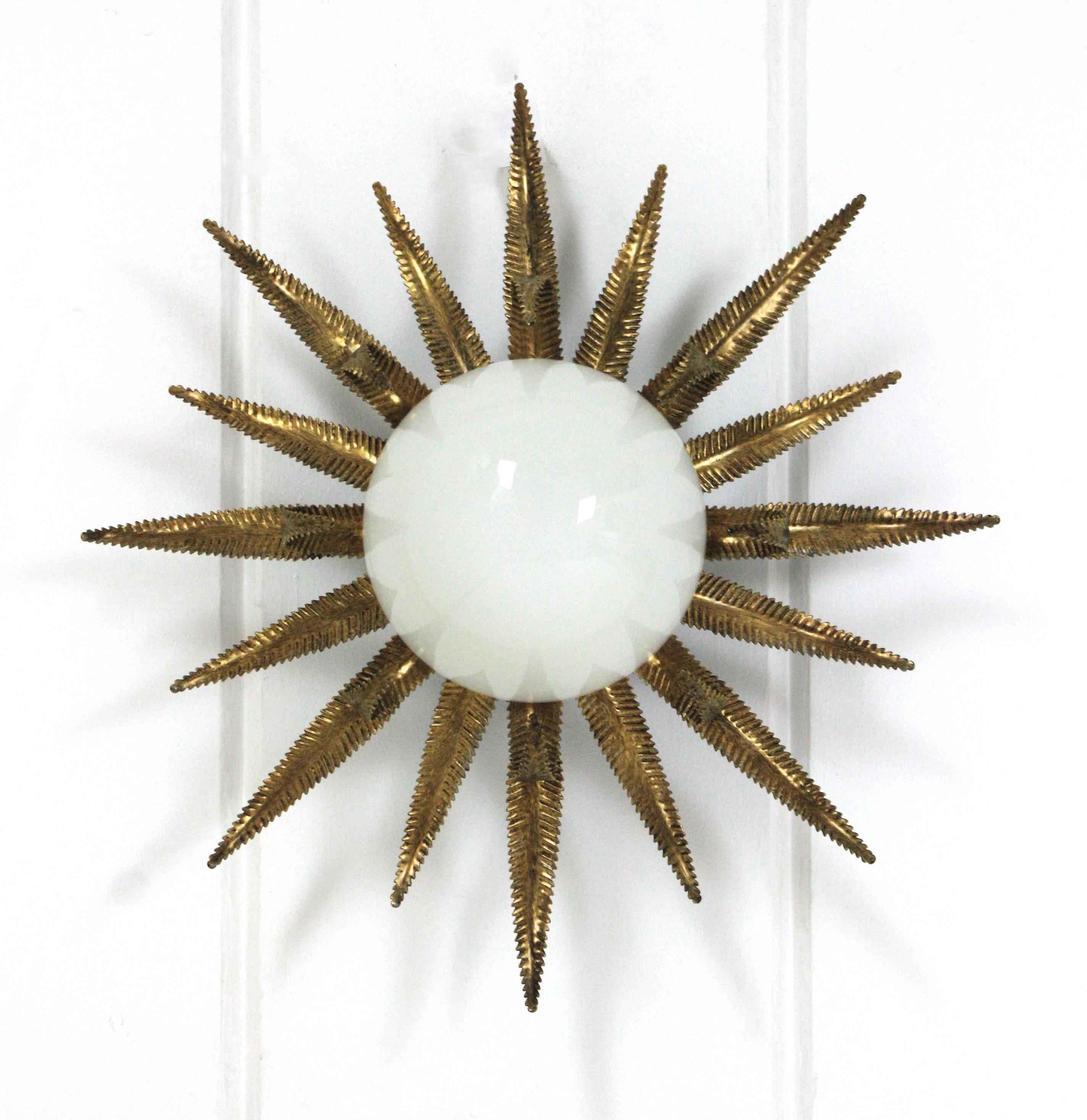 Outstanding French sunburst flush mount in gilt metal and milk glass, 1950s
This Sunburst starburst ceiling light fixture has an eye-catching construction. The sunburst backplace in patinated gilt iron and sunburst or starburst shape holds an