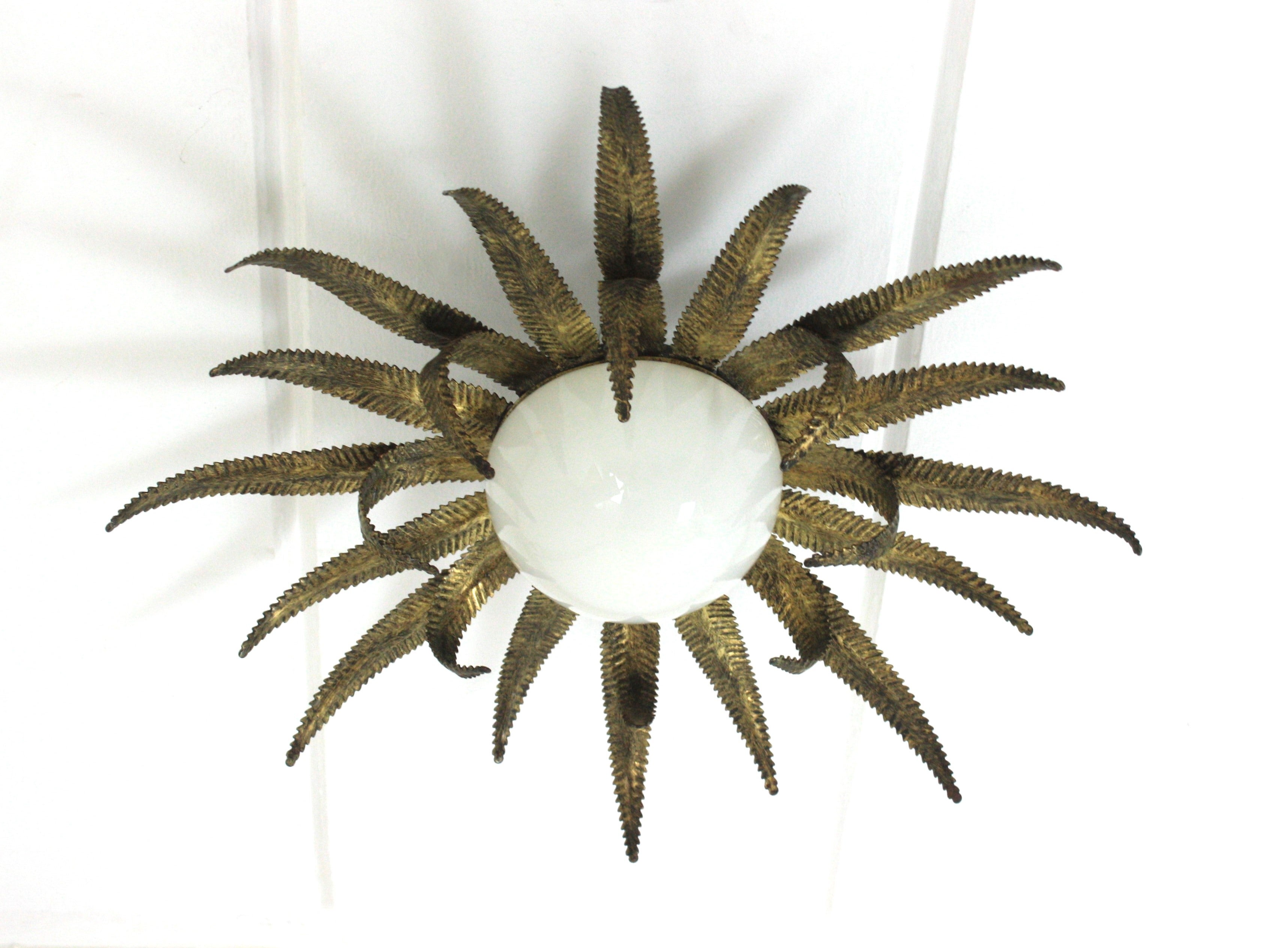 Outstanding French sunburst flush mount in gilt metal and milk glass, 1950s
This Sunburst starburst ceiling light fixture has an eye-catching construction. The sunburst backplace in patinated gilt iron and sunburst or starburst shape holds an
