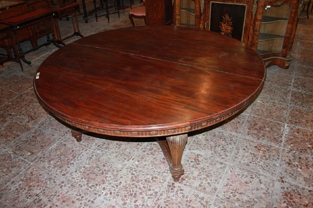 Large French table from the early 1800s, Louis XVI style, made of mahogany wood. It has a closed diameter of 2 meters, extendable to 4.20 meters, with the tabletop border finished with carved motifs, and it ends with a substantial stretcher uniting
