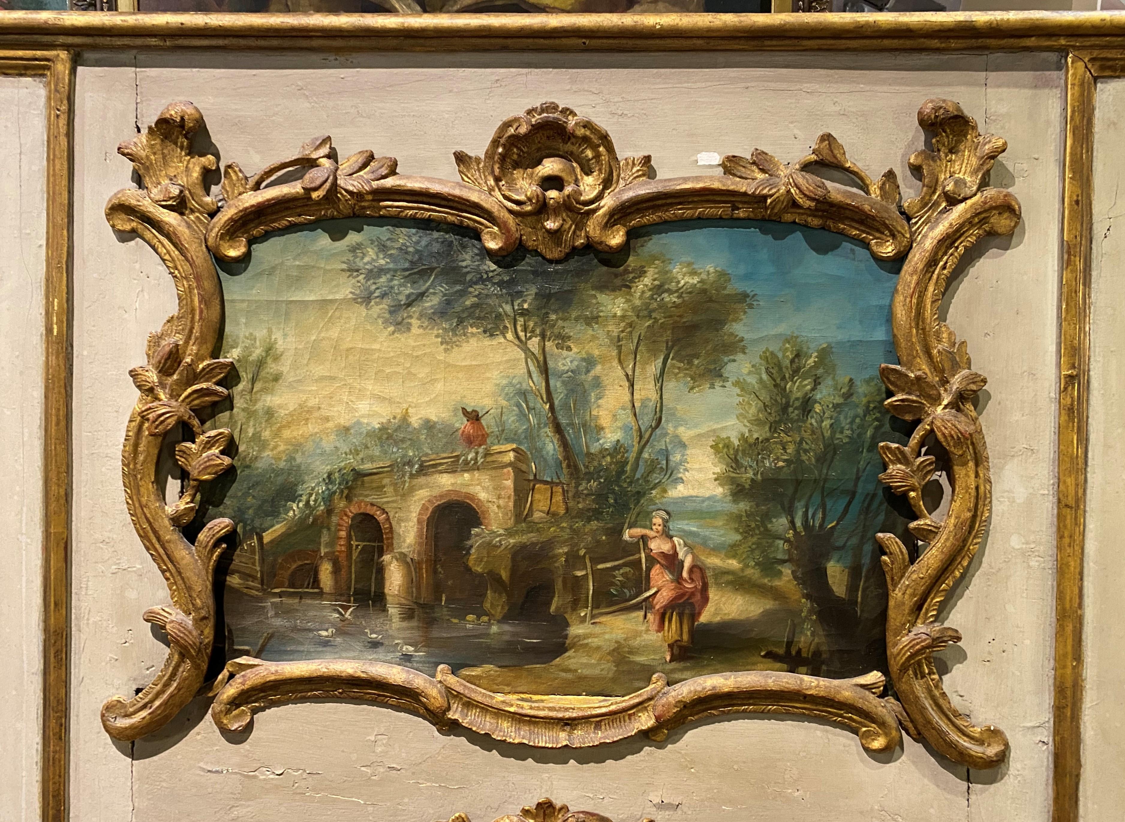 A fine large Trumeau over mantle mirror with a hand painted French genre scene with a woman and an arched bridge, with an applied gilt scrollwork surround, over a vertical mirror with carved gilt surround. The mirror is French in origin, dating to