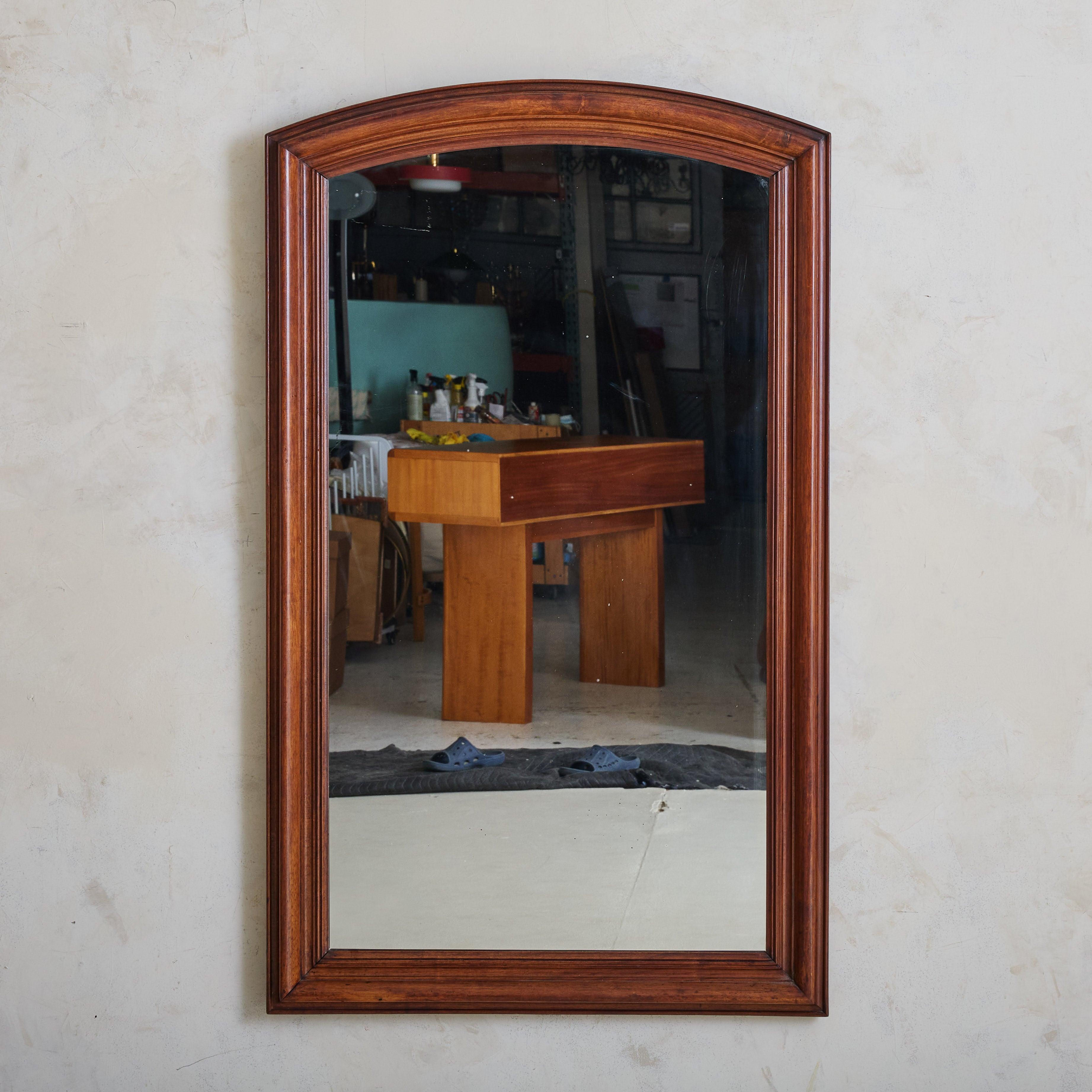 Crafted in France over one hundred years ago, this early 20th-century mirror has a stately arched solid walnut frame accented with hand-carved details. At 4.5 feet tall, the mirror’s generous proportions make it well suited to hang above a