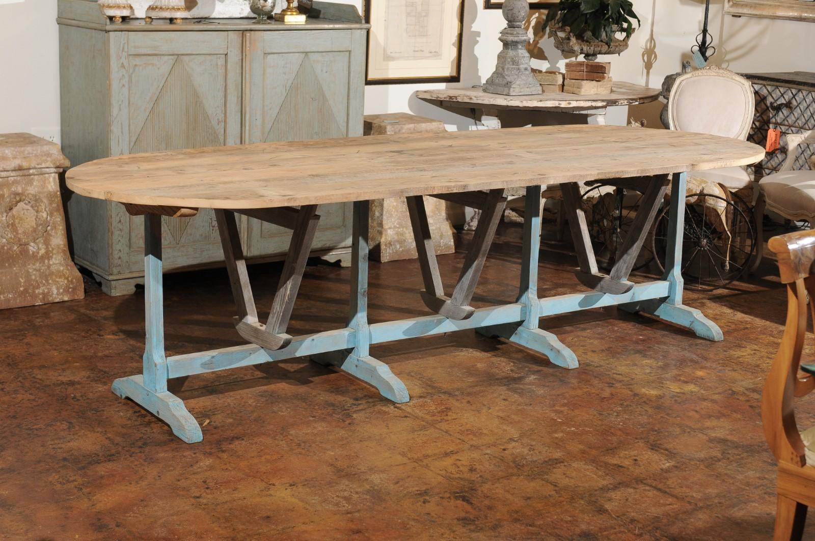 A large French rustic wine tasting table from the 19th century, with oval tilt-top and painted trestle base. Born in France during the 19th century, this large wine tasting farm table features a rustic planked oval tilt-top sitting above a light