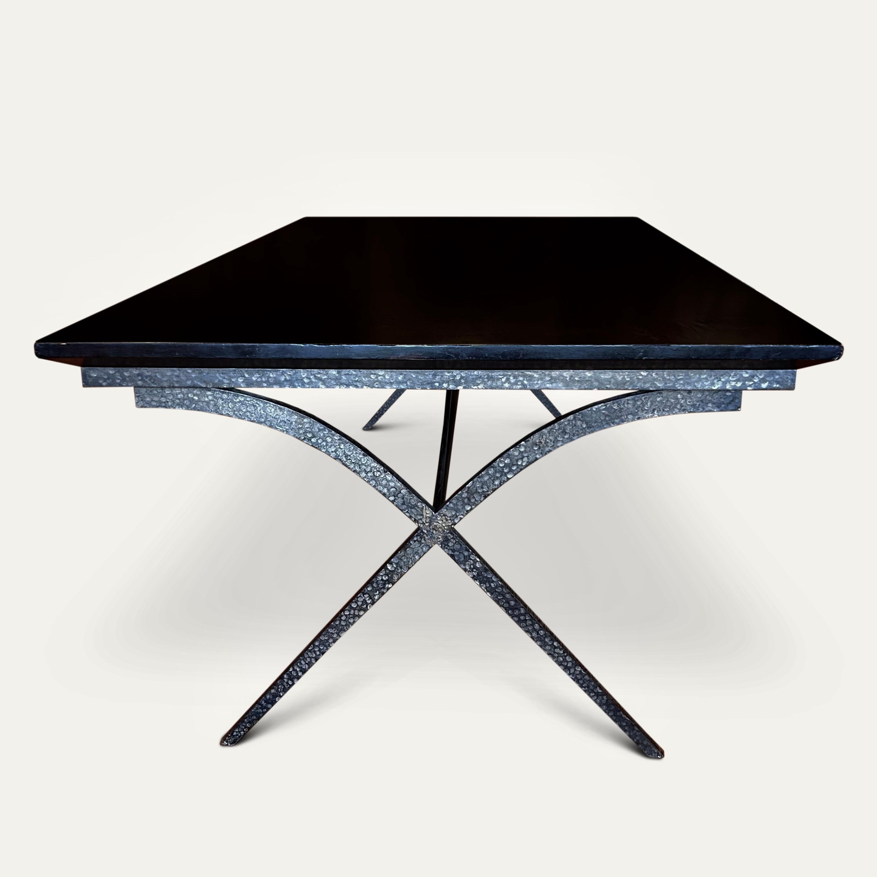 Gran mesa de comedor francesa de hierro forjado sobre una base en forma de x unida con una barra circular extensible, hacia 1930. 
La base y el friso están decorados con círculos puntuados martillados a mano y la mesa acabada con un tablero de