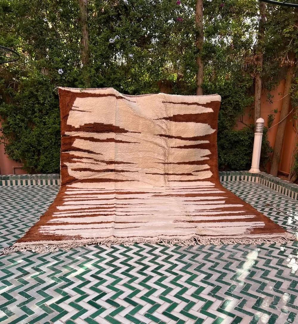 This large, modern handwoven Moroccan rug was made by hand by skilled weavers in the Atlas Mountains of Morocco. It features ultra high quality M'rirt wool, with a neutral cream base and a brown animal-print-esque design along the borders.  This
