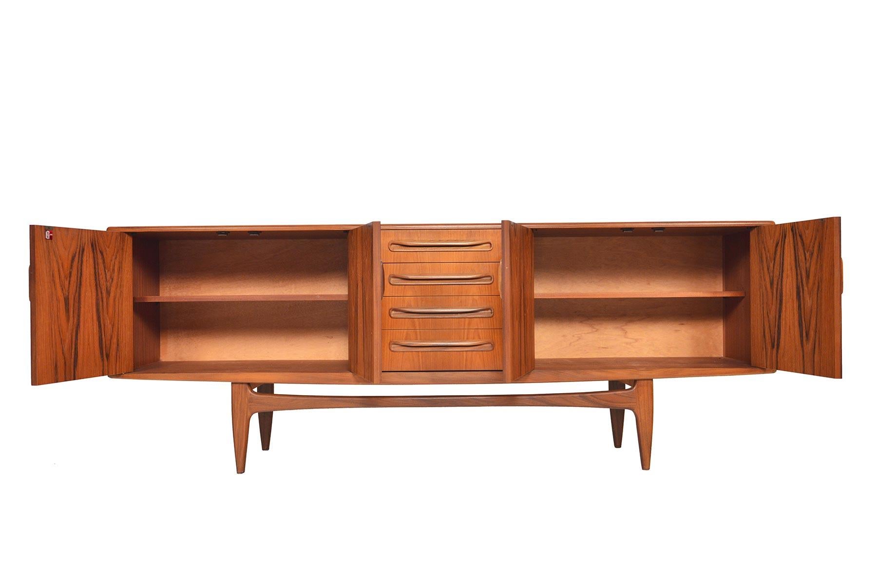 This large Mid-Century Modern G Plan Fresco teak credenza was designed by Victor Wilkins in the 1960s. Beautiful afromosia pulls adorn the drawers and doors of this piece. Left and right doors open to reveal adjustable shelving. Case floats upon a