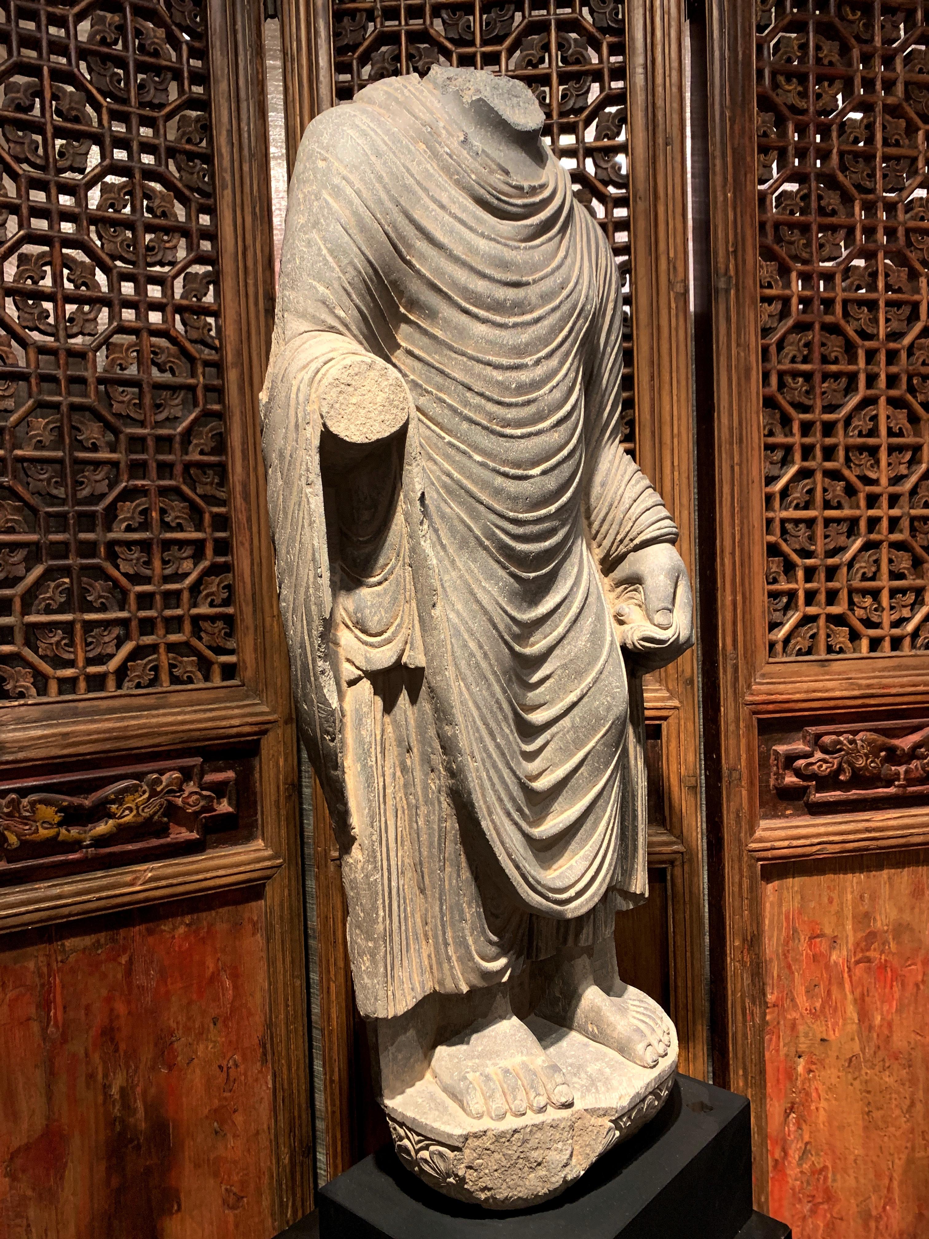 A large and powerfully carved gray schist Gandharan standing Buddha featuring wonderful drapery, ancient region of Gandhara, circa 2nd - 3rd century. Although missing his head and gesturing hand, this figure can still be identified as the historical