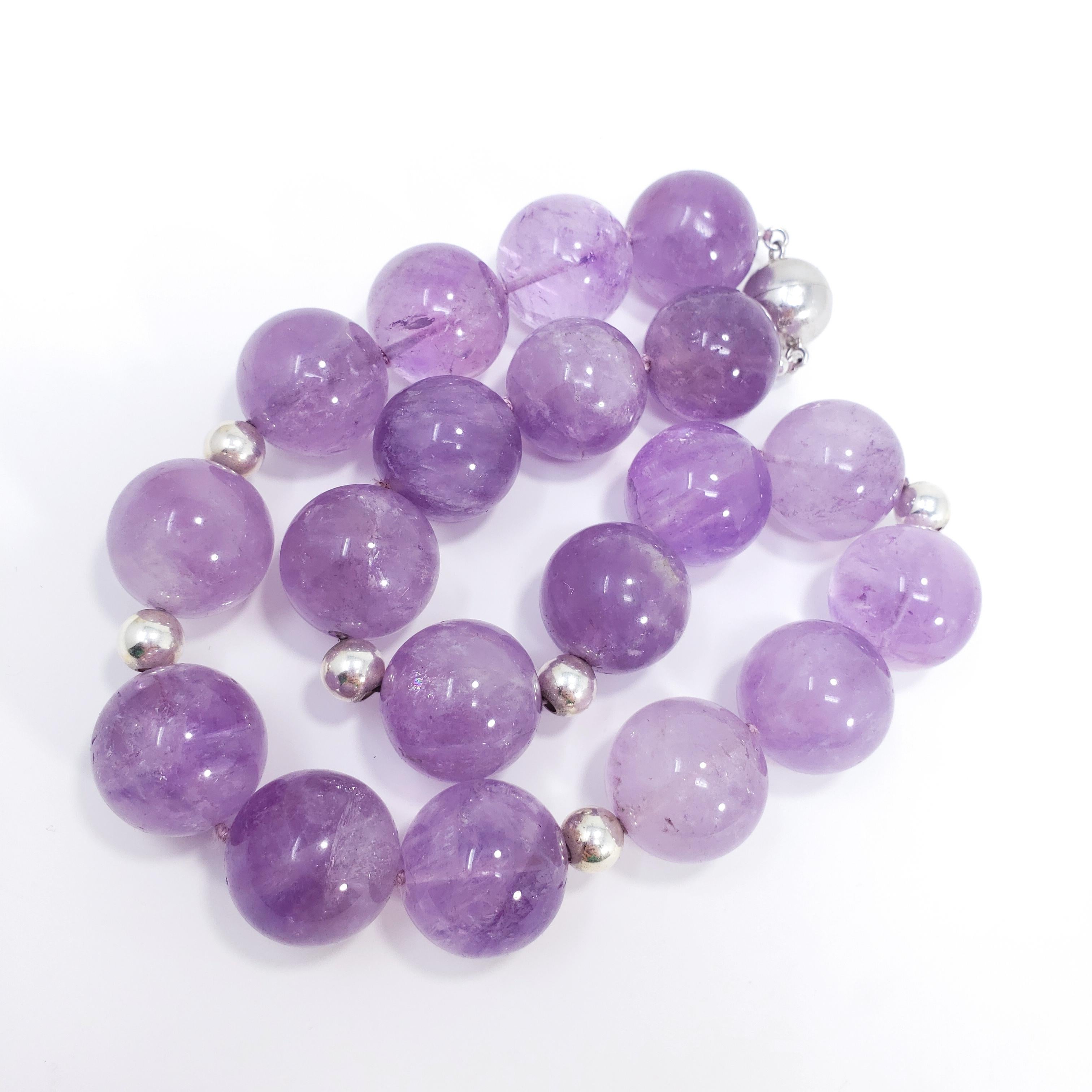 An elegant amethyst necklace! Features 20mm genuine amethyst beads on a violet-colored knotted string, accented with sterling silver 7.5mm beads. This princess-length necklace is fastened with a magnetic sterling silver ball clasp for a