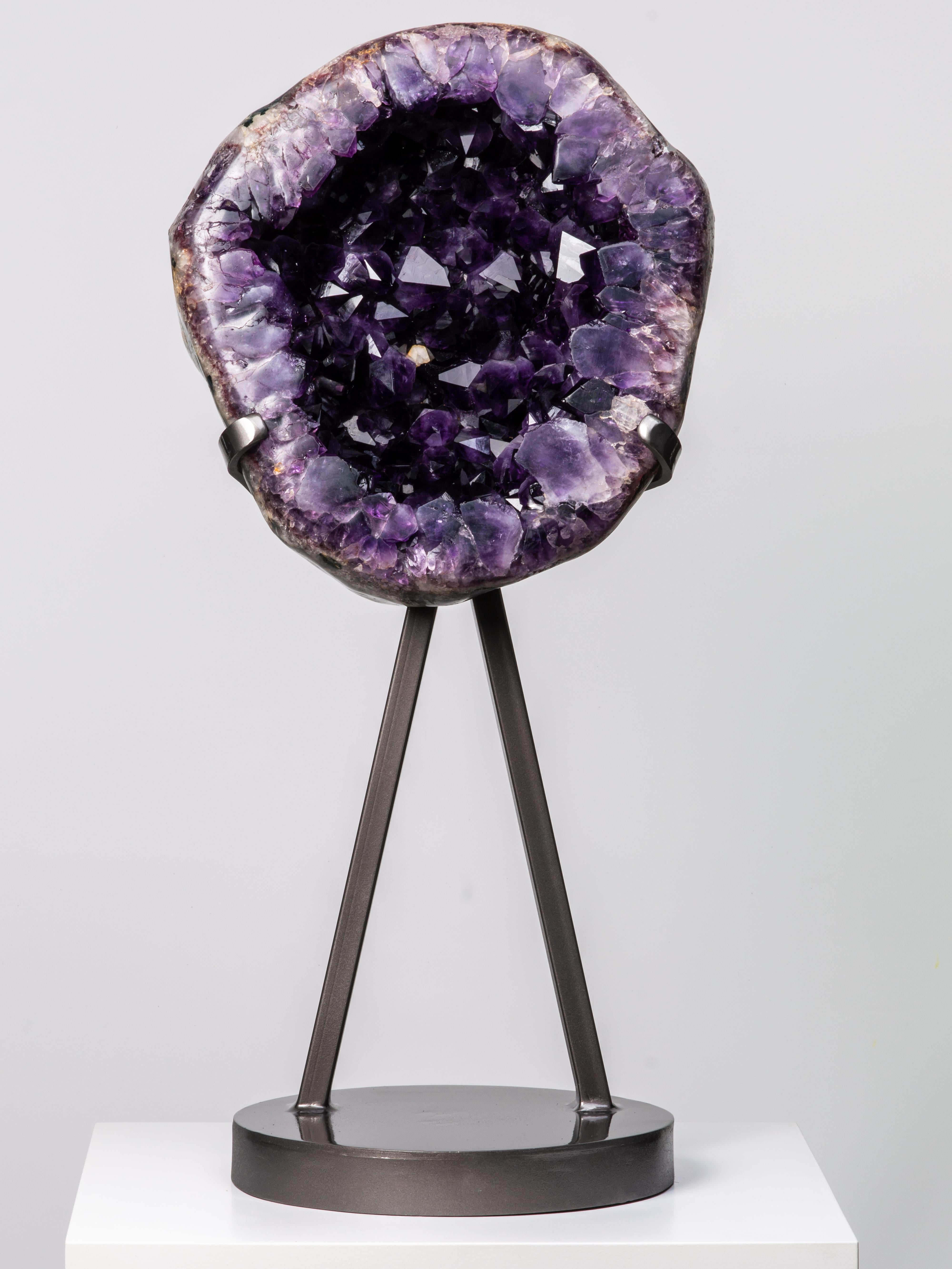 A striking geode slice with very high peaked deep purple amethyst crystals. The
thick, prominent crystals allow us to appreciate the intense cloudy quality of the
finest amethyst. A small creamy calcite can be found to the interior. The
