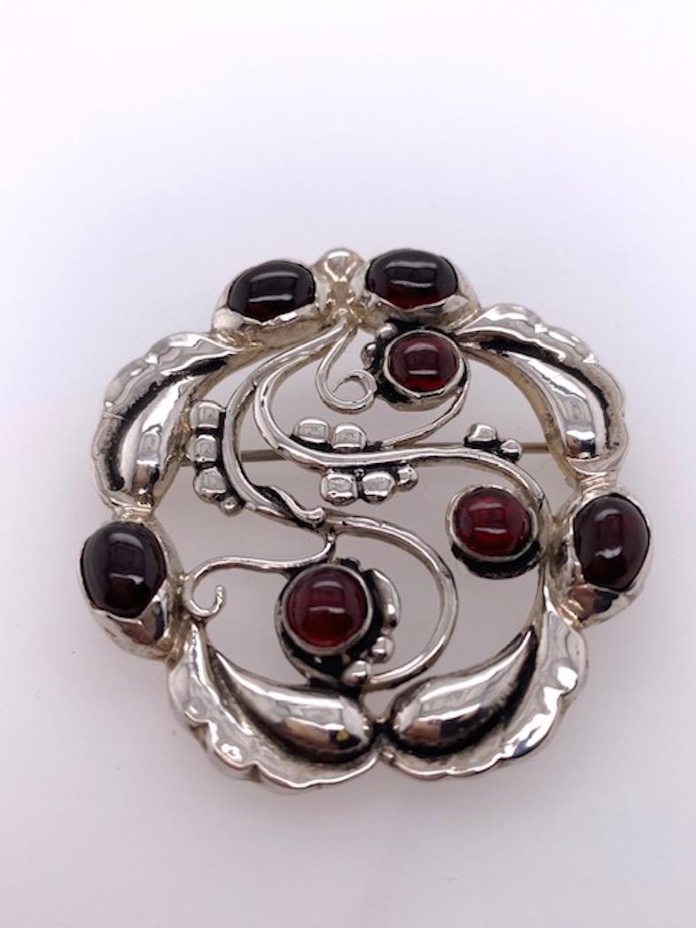 Very graceful sterling silver brooch.  Made and signed by GEORG JENSEN.  Set with seven bright cabochon garnets.  Lovely scalloped border.  1 3/4