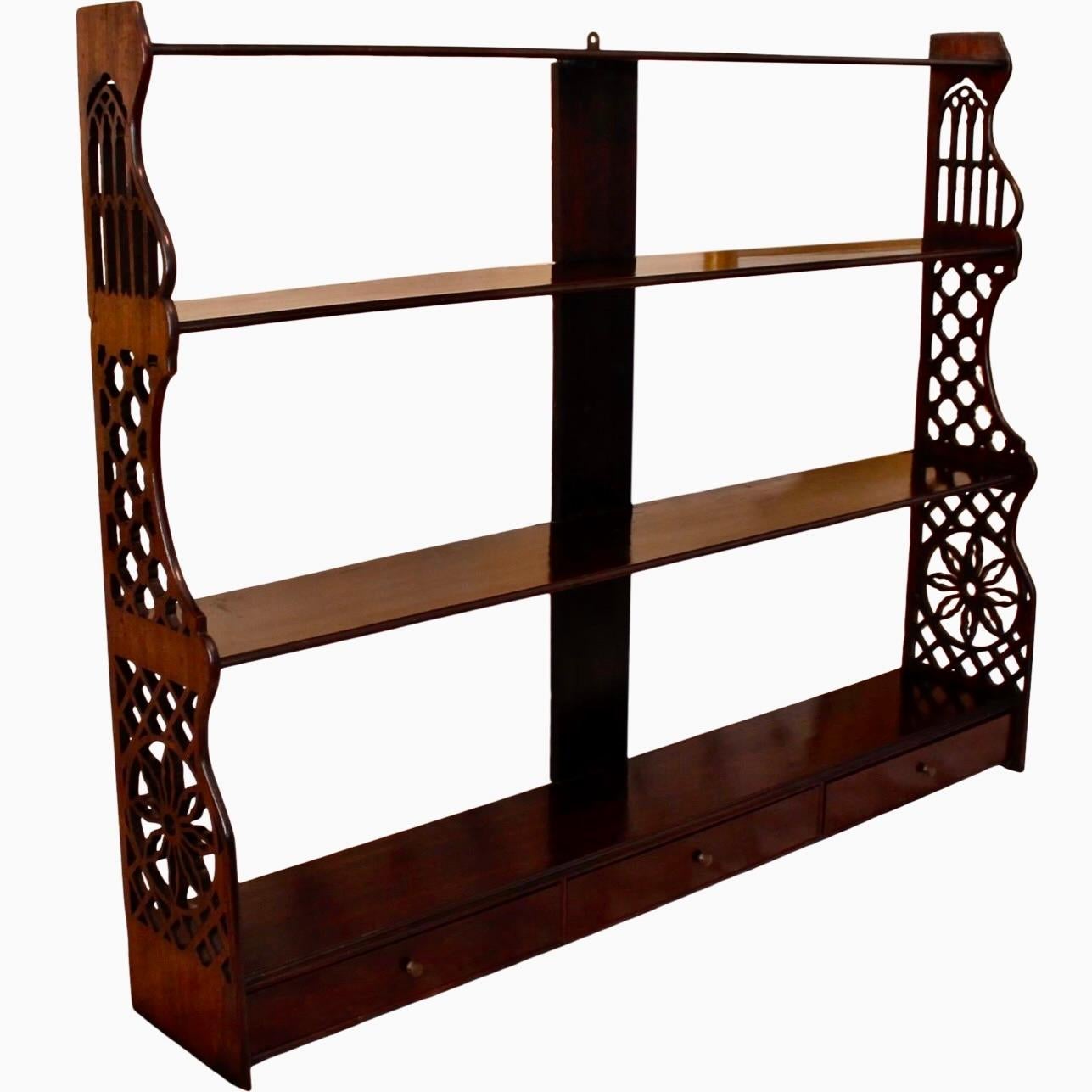 A fine George III period hanging shelf with fretwork sides and three drawers at the bottom. Four shelves are enlivened by different fret design at each level, the uppermost fitting Neo-Gothic tracery into the tapering silhouette off the sides. Good