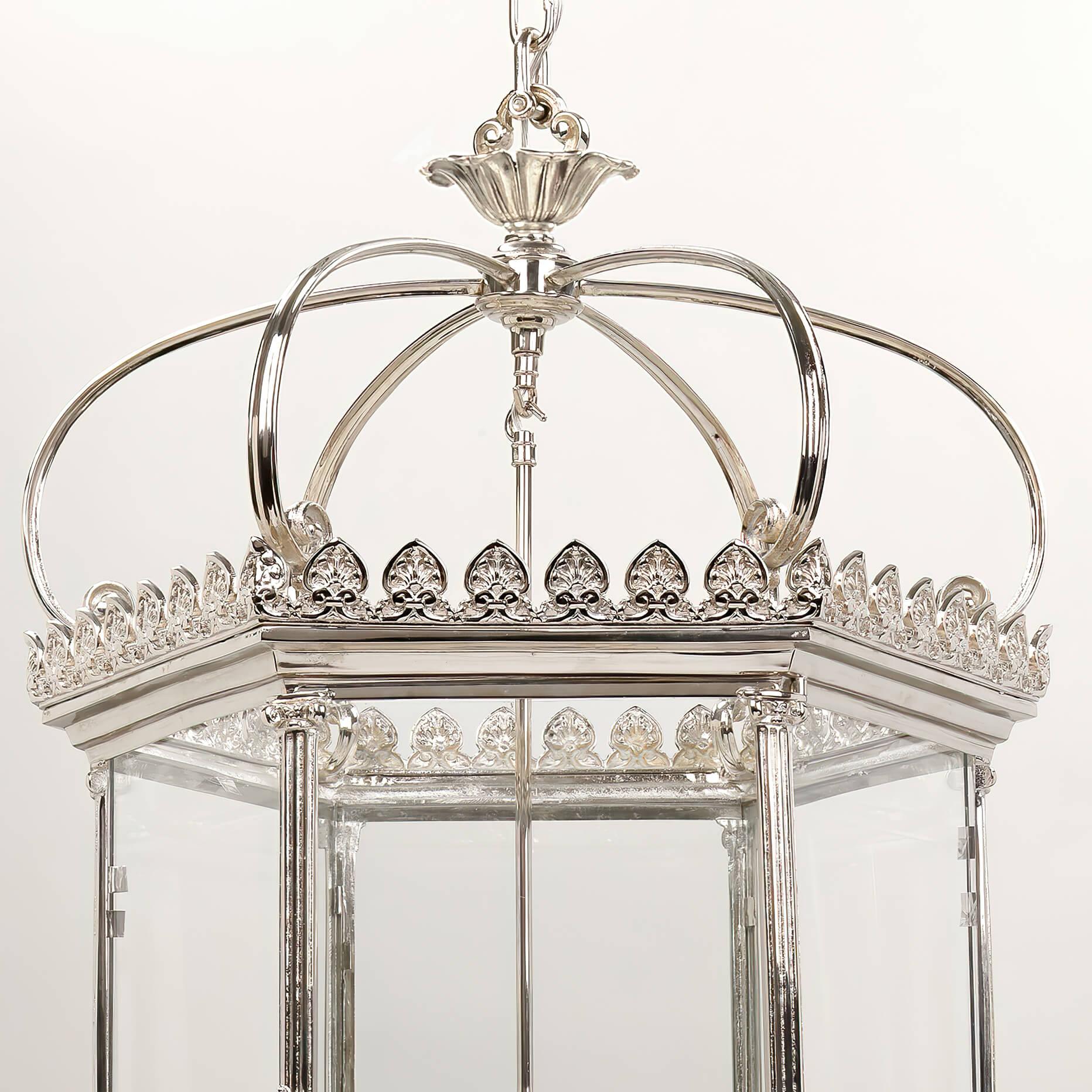 A Grand Georgian style hexagonal six-light hall lantern with a nickel finish and a regal crown above a Fleur-de-Lis decorated gallery with six glass panels, an opening door, framed by Roman Ionic columns with drop finials.

Dimensions: 25