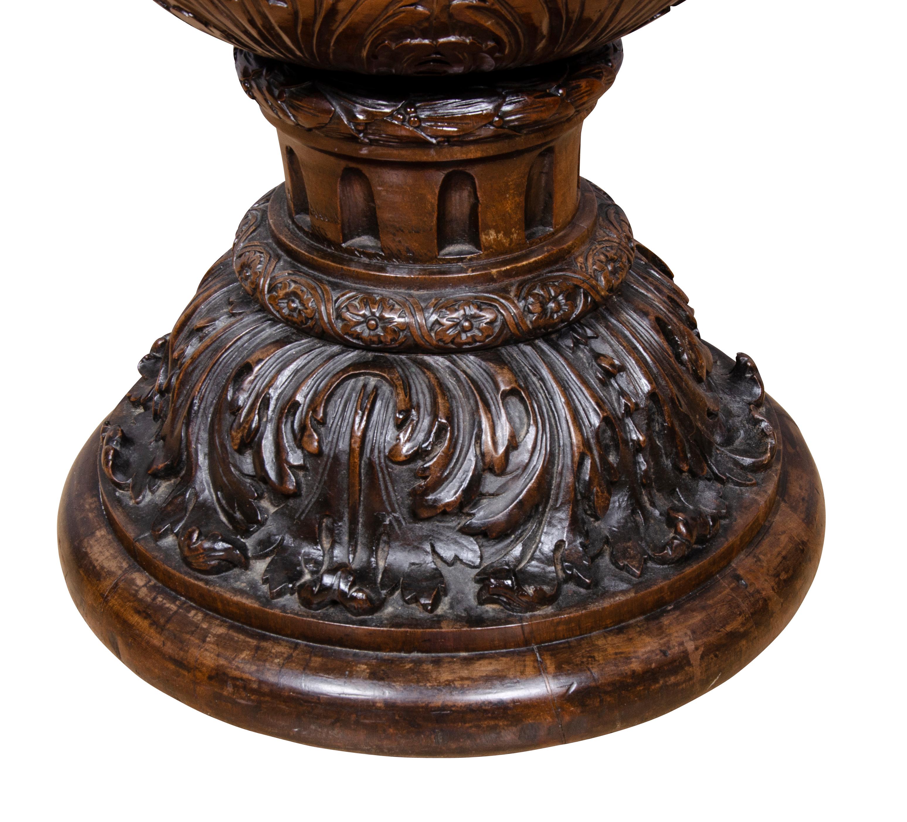 Shaped like a goblet. Tapered form carved and hollowed from a single piece of wood, the exterior decorated with a bacchanalian parade of figures of Pan playing instruments on and pulling a wagon, grape leaves and merriment, lower section of urn with