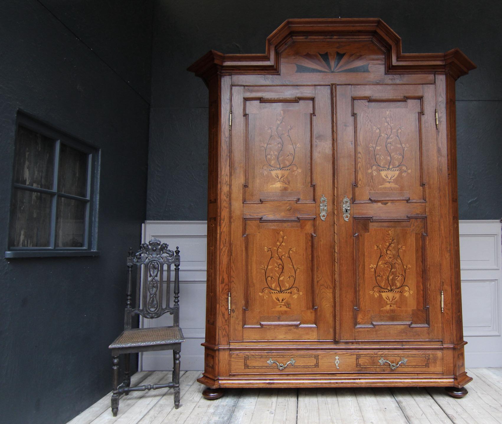 Large representative hall cupboard from the 19th century. Probably from Hesse. Solidly made of oak with inlays of maple, walnut and other precious woods.

Two-door corpus with bevelled corners standing on four squashed ball feet, base level with