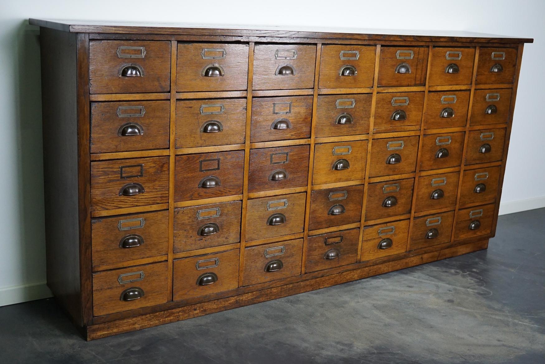 This apothecary cabinet was made circa 1930s in Germany. It features 35 decent sized drawers with cup handles and name card holders. The interior dimensions of the drawers are: DWH 35 x 24 x 14 cm. The cabinet retained a nice and rich patina over