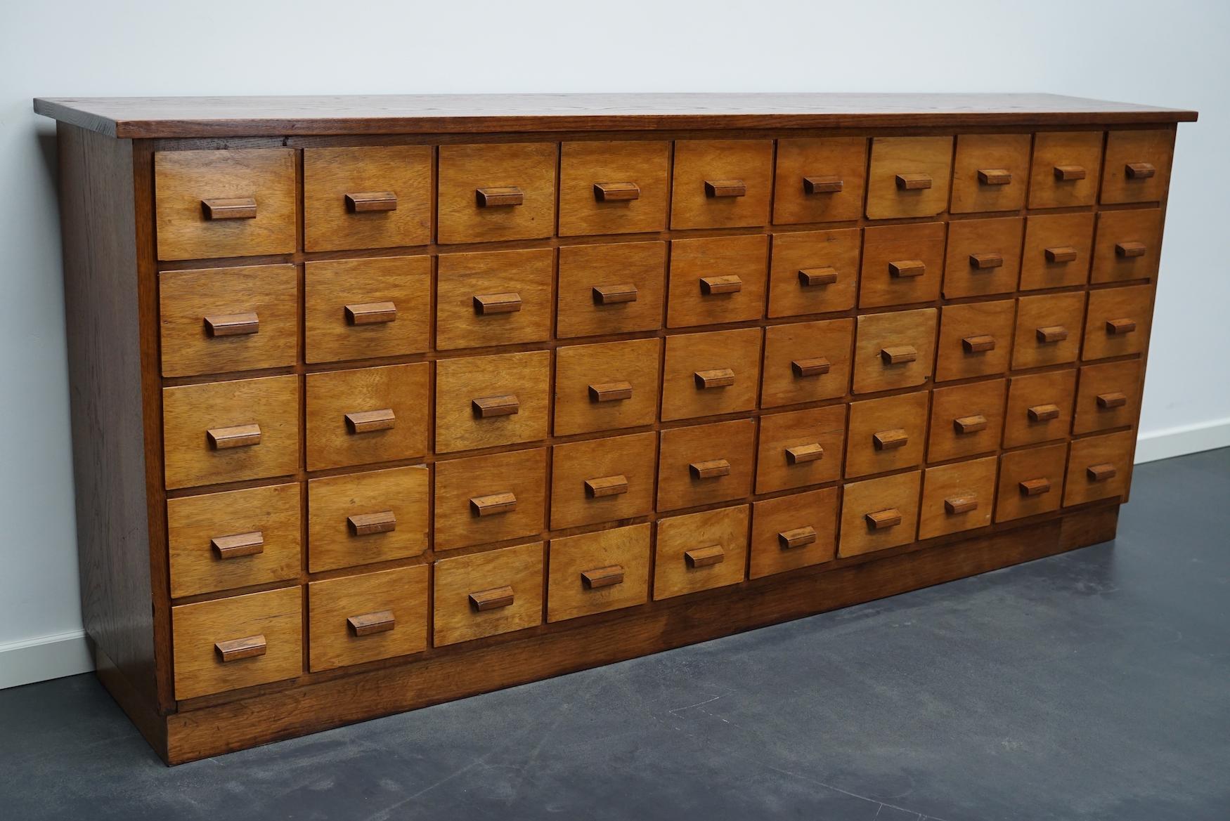 This apothecary cabinet was made circa 1950s in Germany. It features 50 drawers with oak handles. The interior dimensions of the drawers are: D x W x H 33 x 15 x 11 cm.