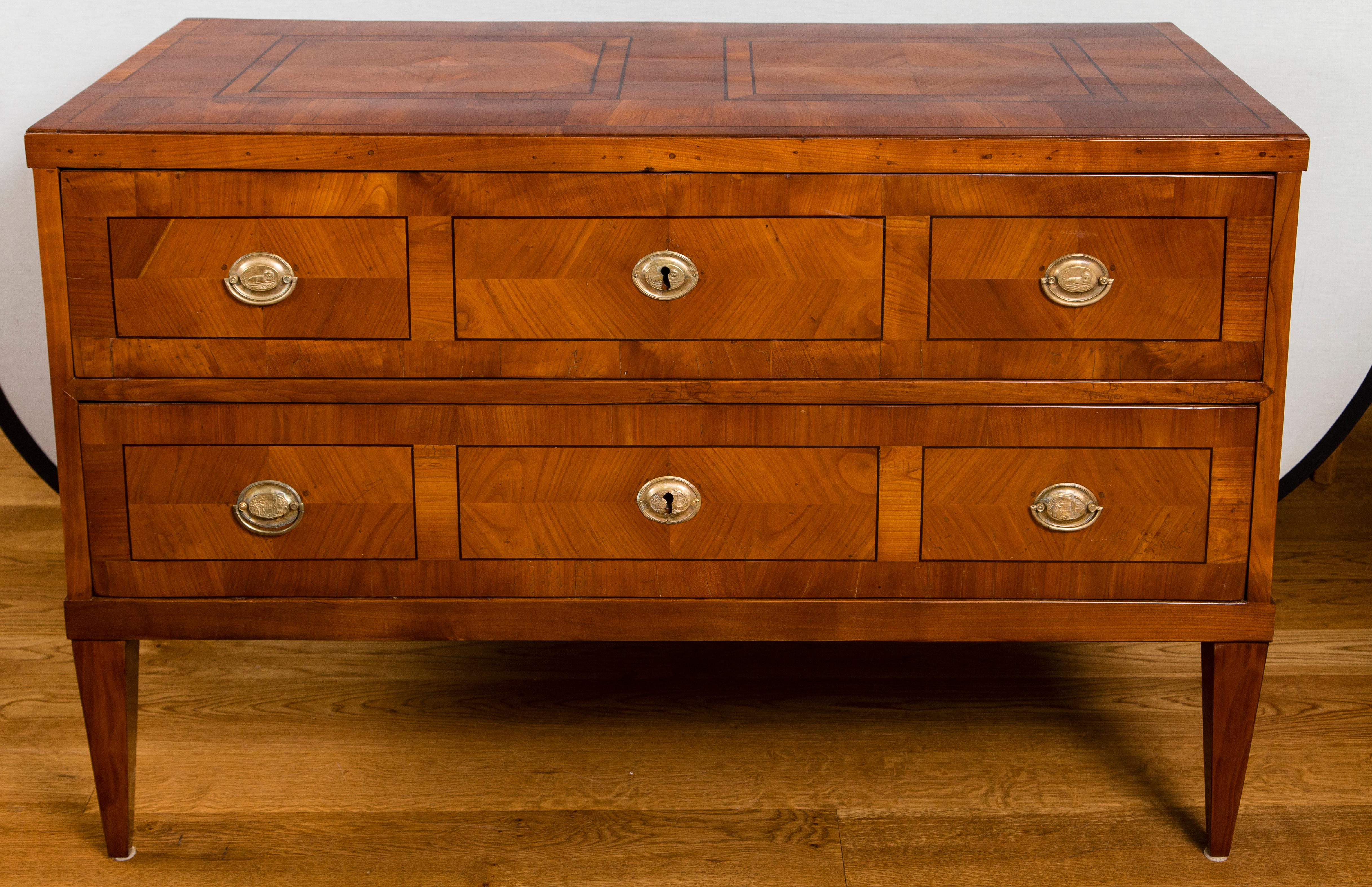 Large neoclassical cherrywood veneer chest with geometric paneled front and plateau comprised of two long drawers opening with antique brass pulls subtly detailing resting lions and finishing on high, straight and tapered legs
Dating: circa