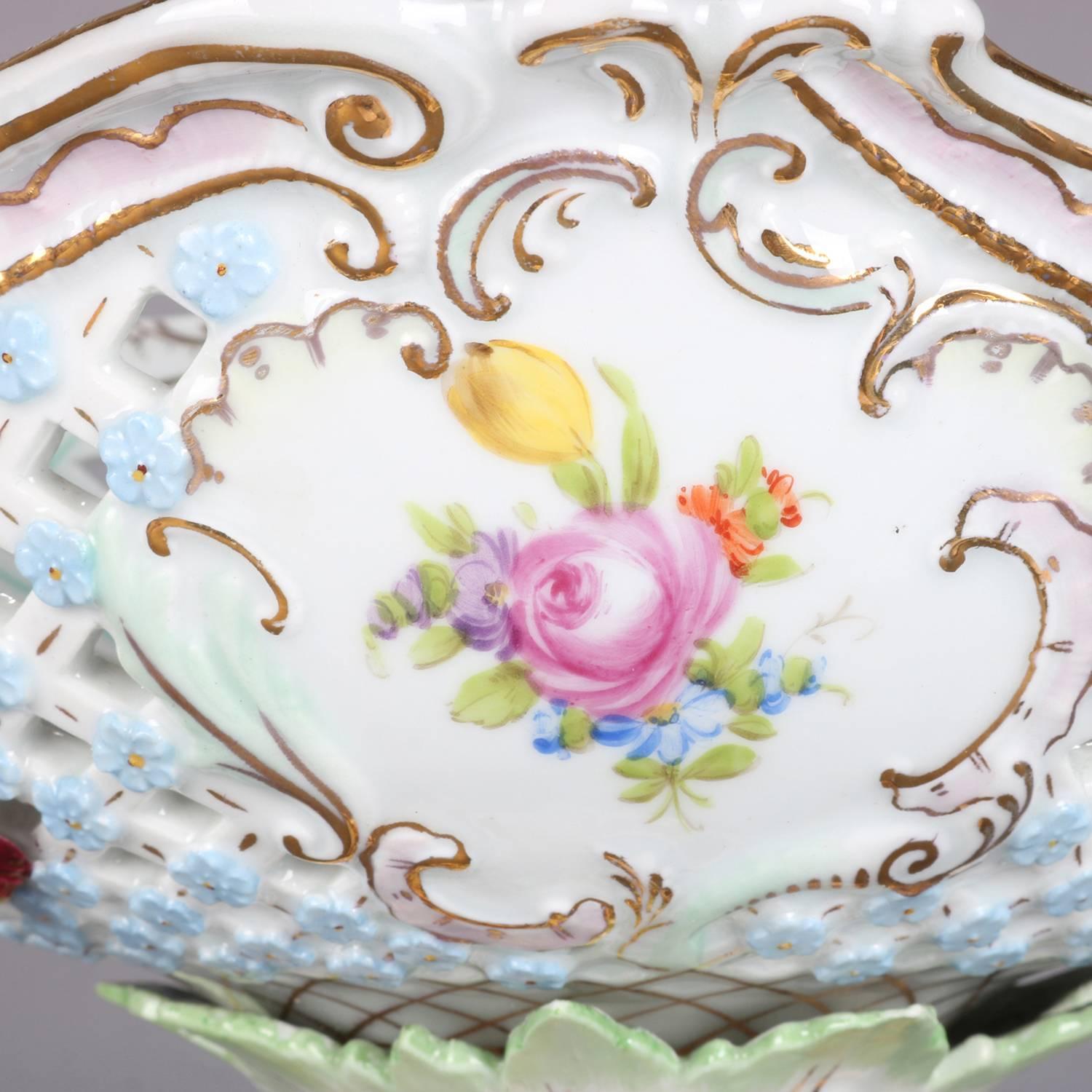 Oversized antique German Dresden porcelain figural hand-painted figural compote features pierced basket weave bowl with floral reserves and applied flowers raised on foliate form column reminiscent of a tree trunk with applied cherub and floral