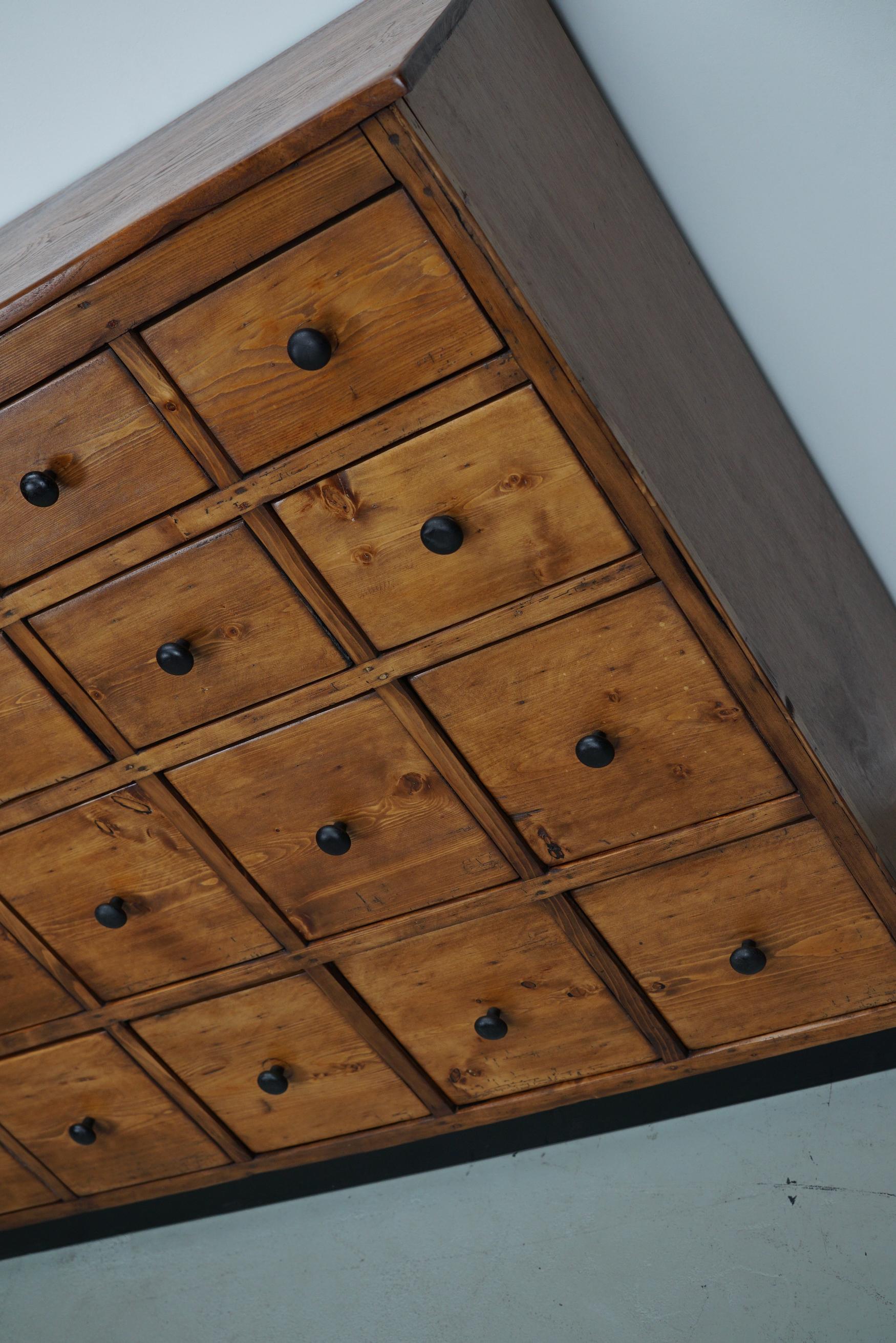 Questo mobile da negozio è stato realizzato in legno di pino in Germania negli anni '50 circa. Presenta molti cassetti con simpatici pomelli rotondi in stile industriale. Le dimensioni interne dei cassetti sono: DWH 33 x 22,5 x 13, 15 e 22,5 cm.