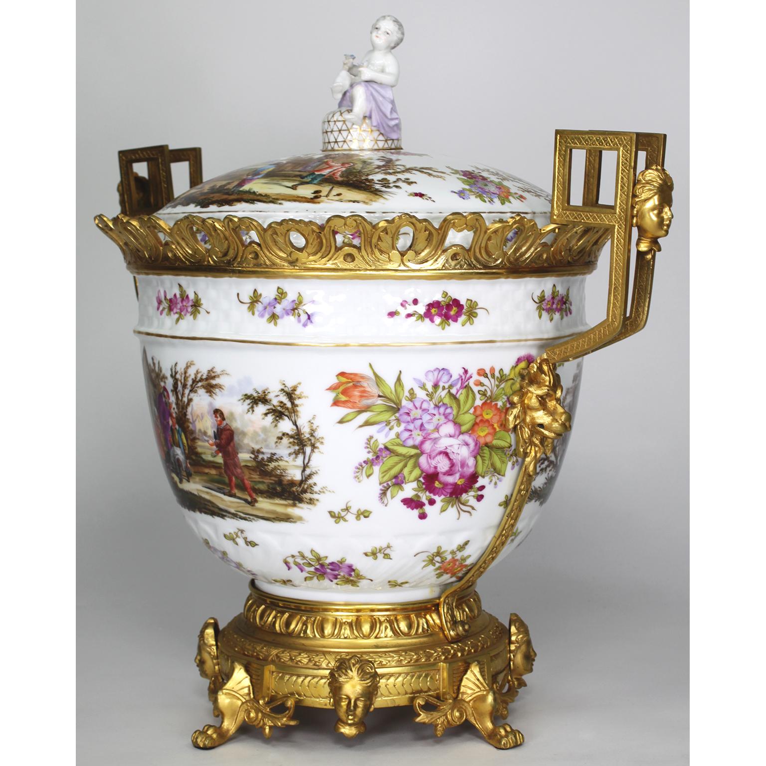 A Large German 19th/20th century Figural Porcelain and Gilt-Bronze Mounted Urn with Cover in the Manner of Meissen. The ovoid porcelain hand painted urn decorated with scenes of festive villagers and elders. The lid also decorated with festive
