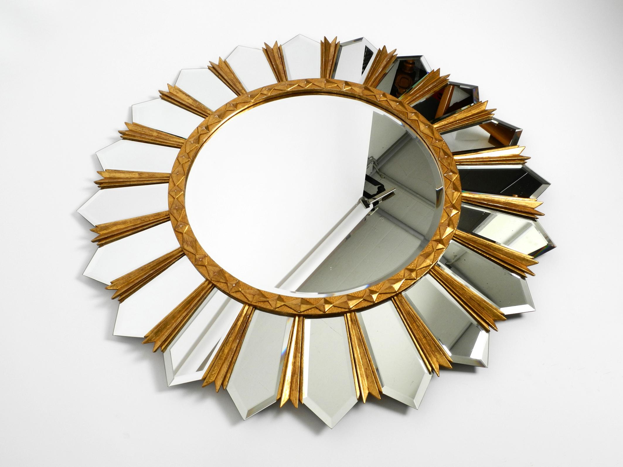 Huge gilded XXL Regency sunburst wall mirror.
Beautiful Italian design from the 1980s.
Very high quality and heavy handcrafted. Lots of nice details.
All the wood is gilded on the front. The round mirror inside is faceted.
The outer mirror parts