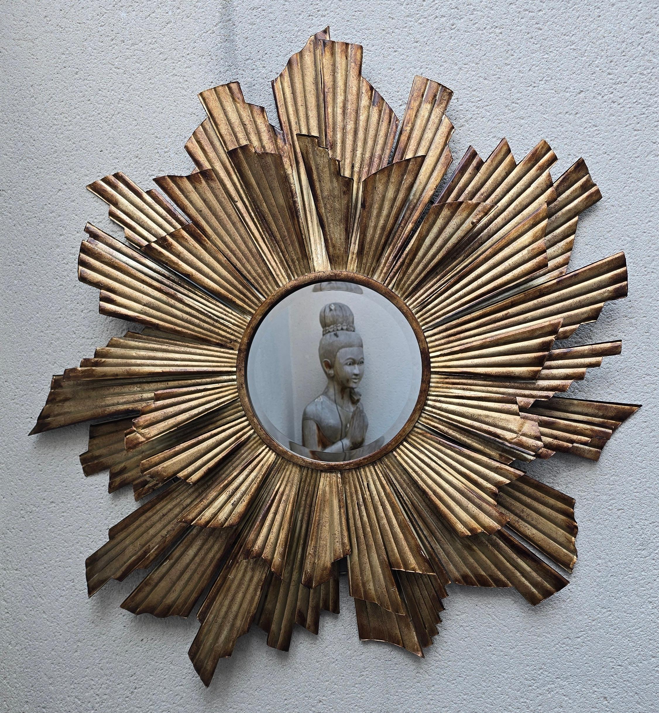 Large Mid-Century gilt metal sunburst mirror from the 1960s with striking pleated rays and a warm patinated finish. A true statement piece that adds Hollywood Regency glamour and timeless elegance to any interior.

Striking vintage sunburst mirror