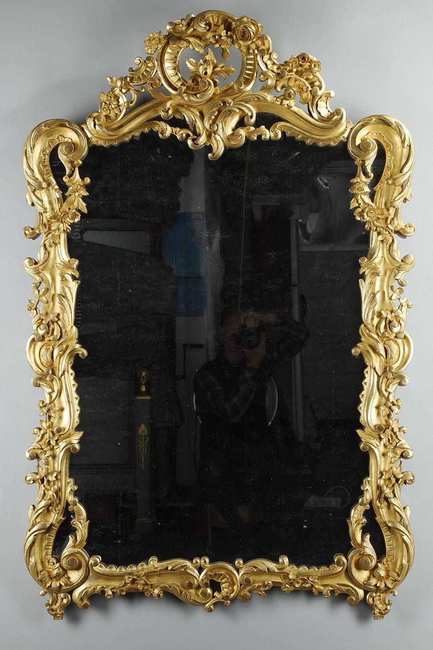 Important rocaille mirror with carved, molded and gilded wood glazing. The decor is decorated with garlands of flowers, acanthus leaves, scrolls and scrolls as well as roses and shells. The large scrollwork glazing beads add more movement to this