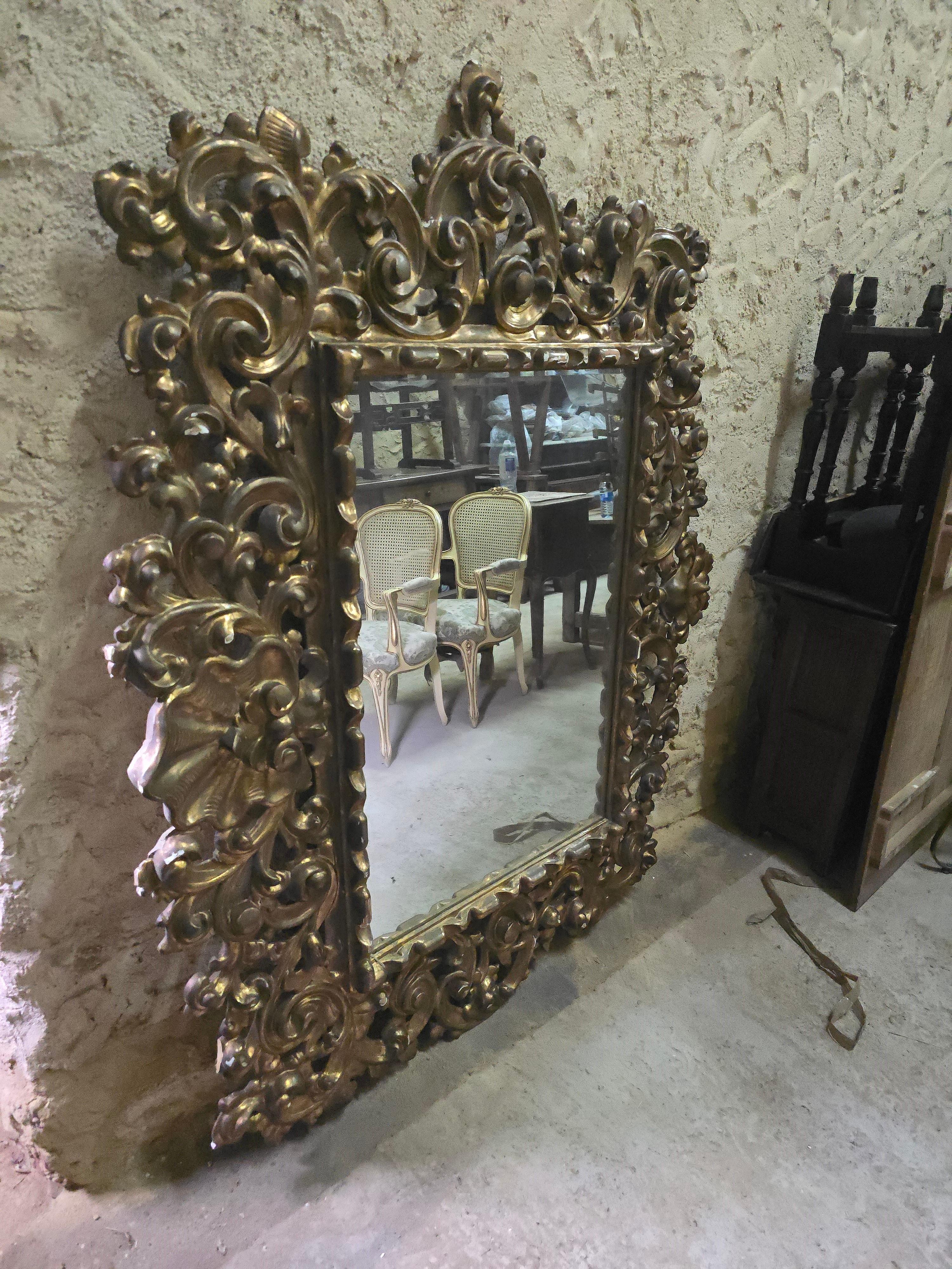 Magnifique miroir italien du XVIIIe siècle, finement sculpté et doré, qui témoigne de l'opulence de l'artisanat de l'époque. Les détails élaborés du cadre en bois reflètent les influences baroques et rococo, avec des motifs floraux complexes et des