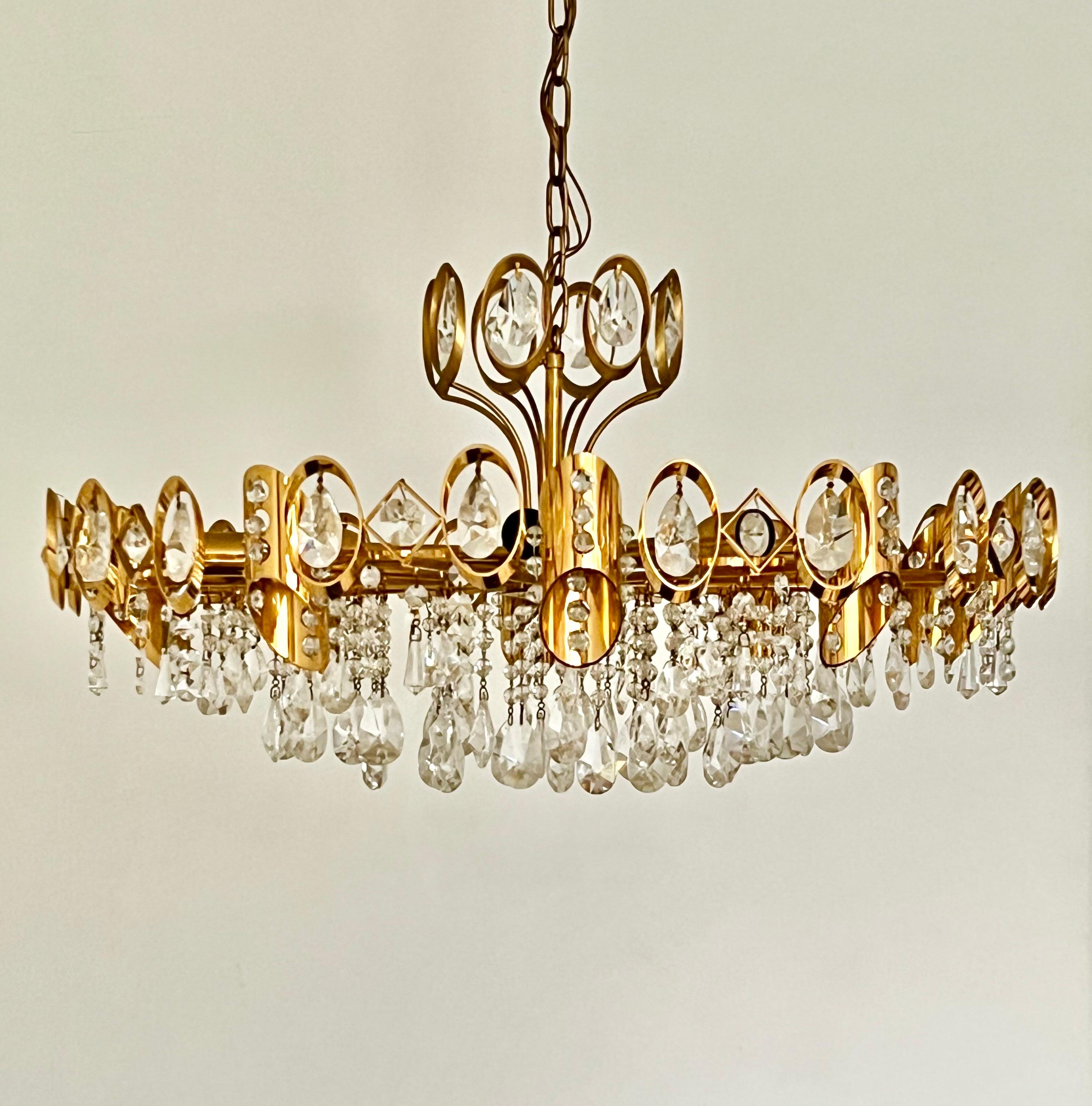 A large gilt-brass chandelier covered in crystal glass droplets, attributed to Palwa. Mid-20th Century, Austria.

A glamorous and very nicely engineered chandelier of good size. The frame is built around ten lateral arms hanging on a chain of