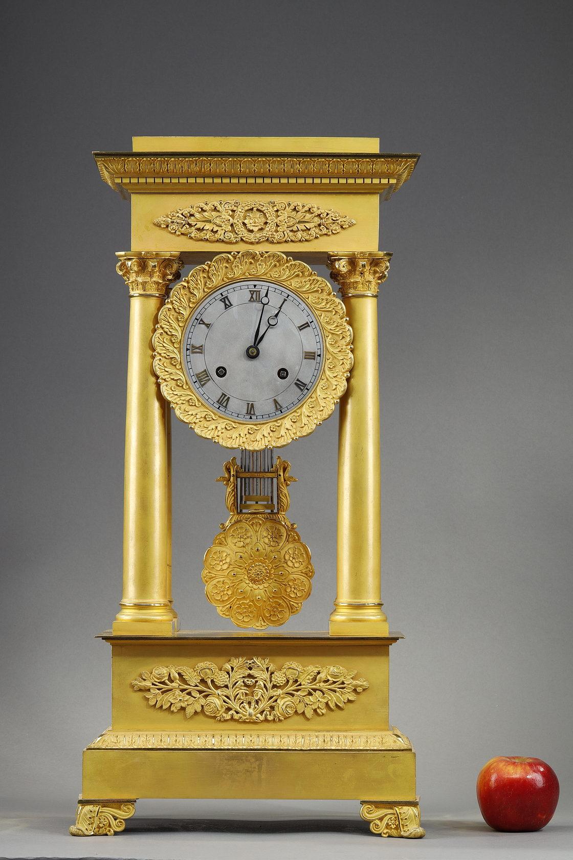 Large gilt bronze portico regulator clock from the Restauration period. It takes the form of an antique architecture with four smooth Corinthian columns with acanthus leaf capitals. The facade features rose, rosette and palmette motifs. The base and